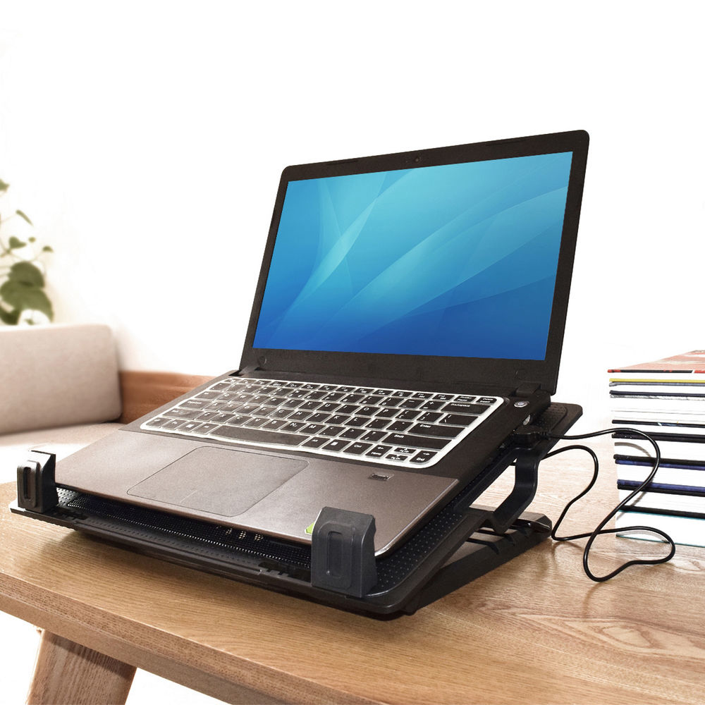 Laptop auf schwarzem Ständer, auf einem Holztisch. Blauer Bildschirm, Tastatur sichtbar. Bücher und Sofa im Hintergrund.