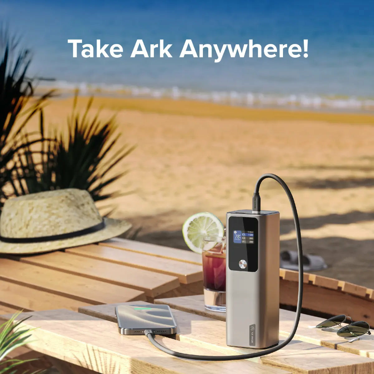 Un power bank carica un telefono su un tavolo di legno. Spiaggia e oceano sullo sfondo.