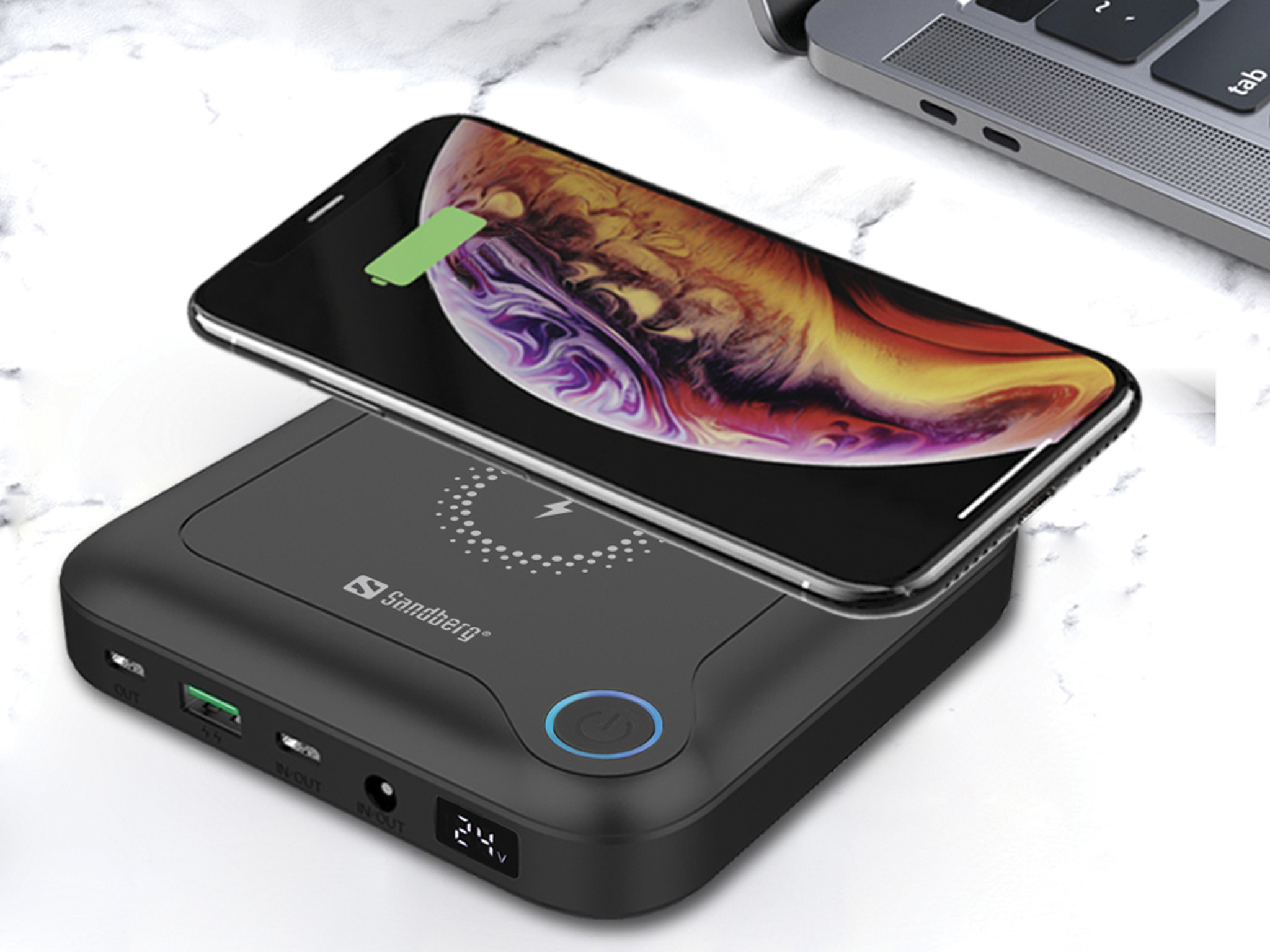 Een telefoon die oplaadt op een zwarte powerbank met een laptop op de achtergrond. De telefoon toont een oplaadindicator.