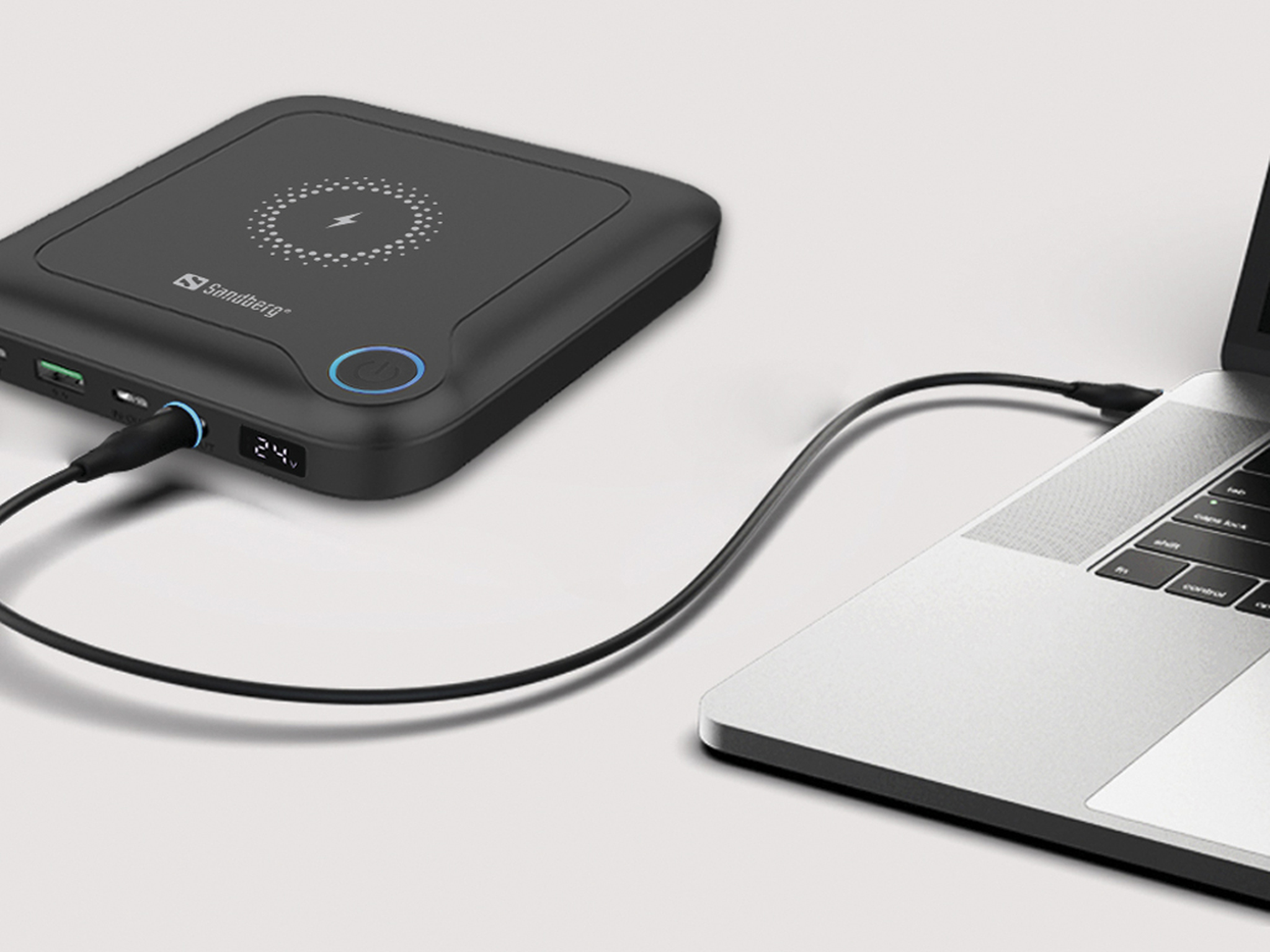 Een zwarte powerbank met een laptop verbonden via een zwarte kabel. De powerbank heeft een blauwe aan/uit-knop.