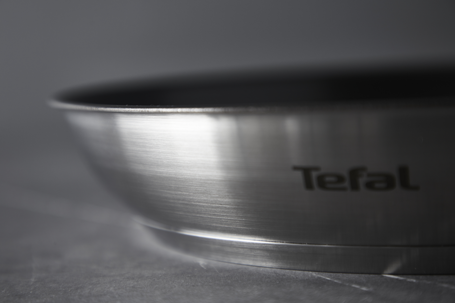 Nahaufnahme einer Edelstahl-Tefal-Pfanne. Die Pfanne ist silberfarben mit schwarzem Innenraum. Der Markenname ist sichtbar.