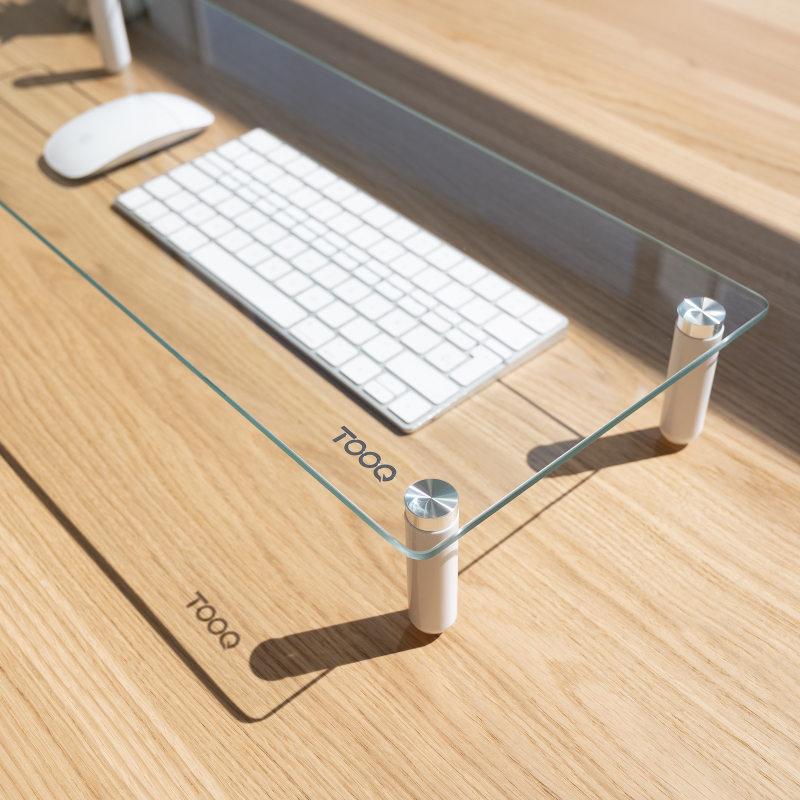 Ein Schreibtisch mit Tastatur, Maus und einem Glasregal mit weißen Zylindern auf einer Holzoberfläche.