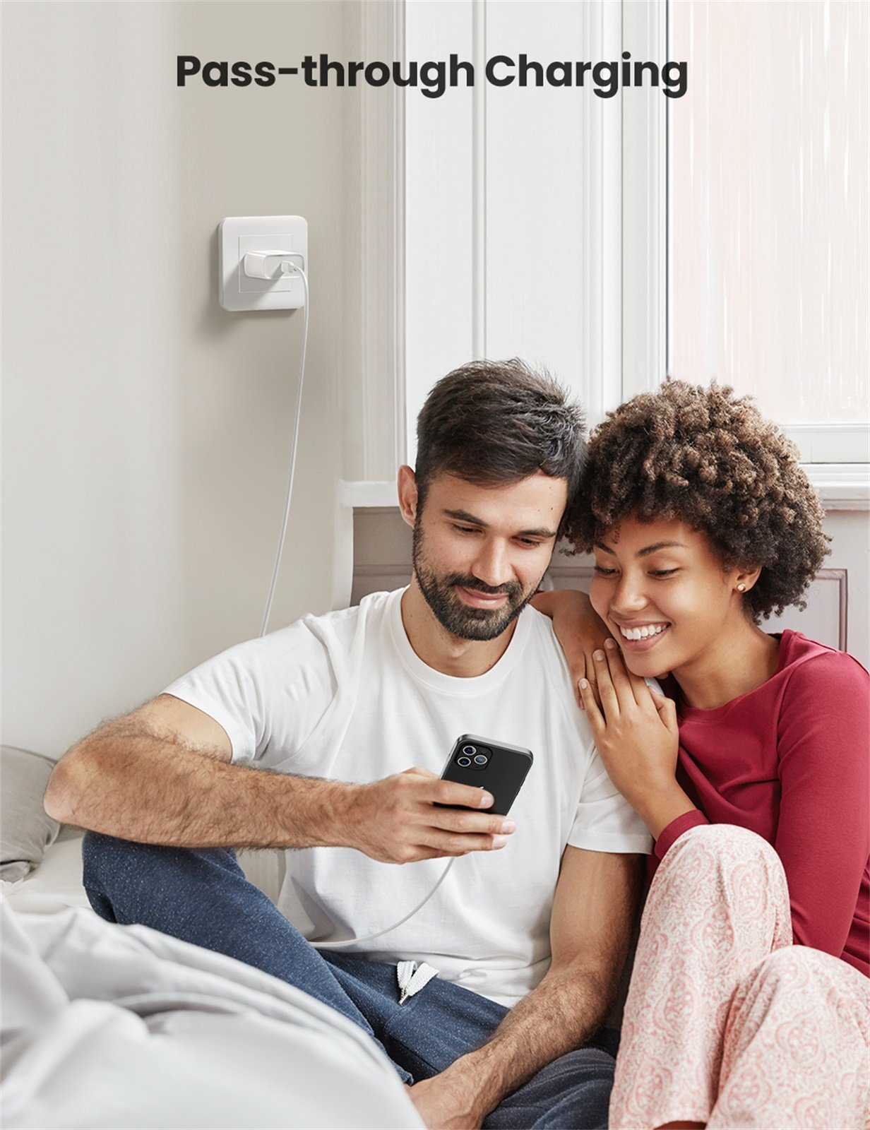 Ein Paar betrachtet ein Telefon; ein Ladekabel ist mit dem Telefon und einer Steckdose verbunden. Text lautet 'Pass-through Charging'.