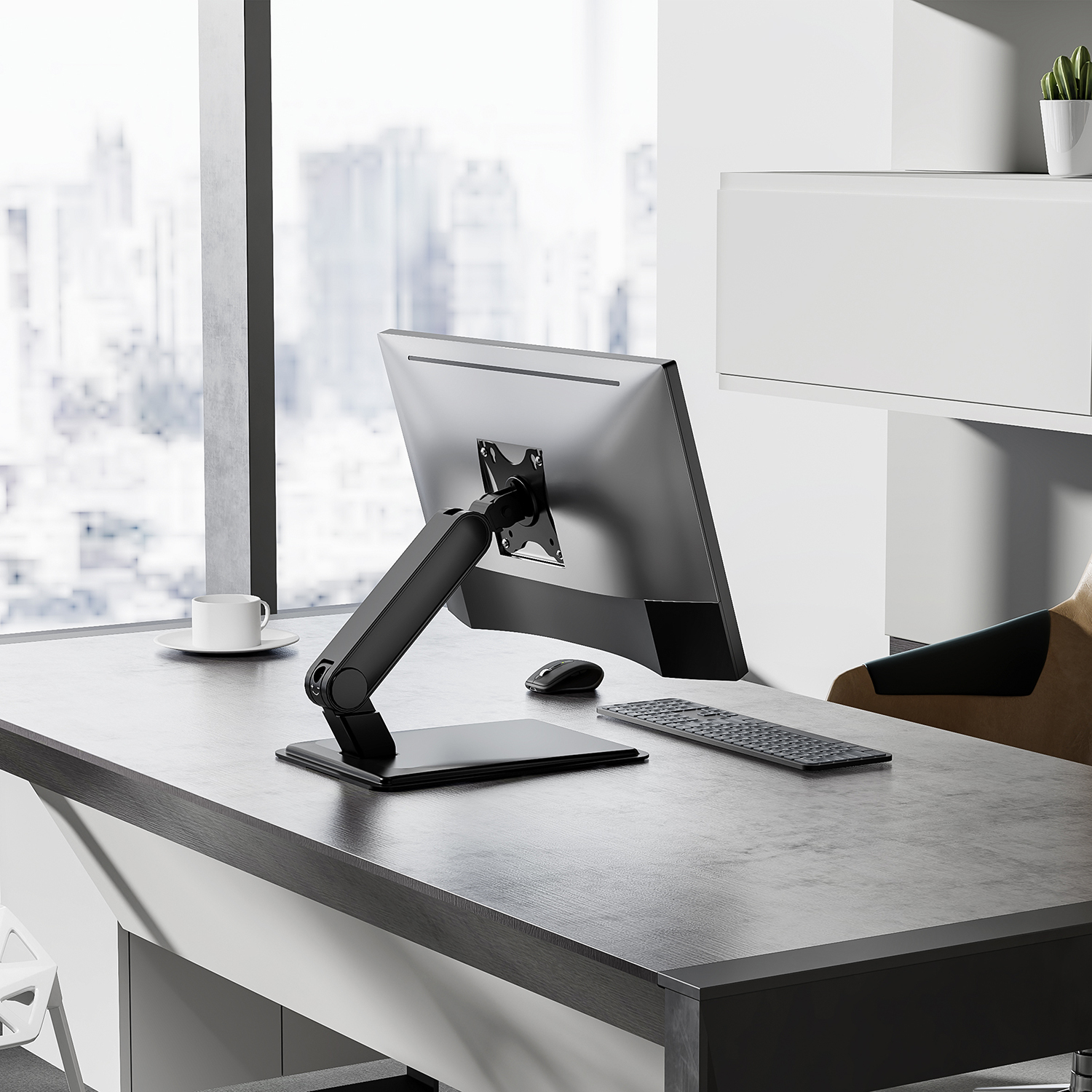 Scrivania con monitor, tastiera e mouse. Una tazza di caffè sulla scrivania. Edifici della città visibili attraverso una finestra.