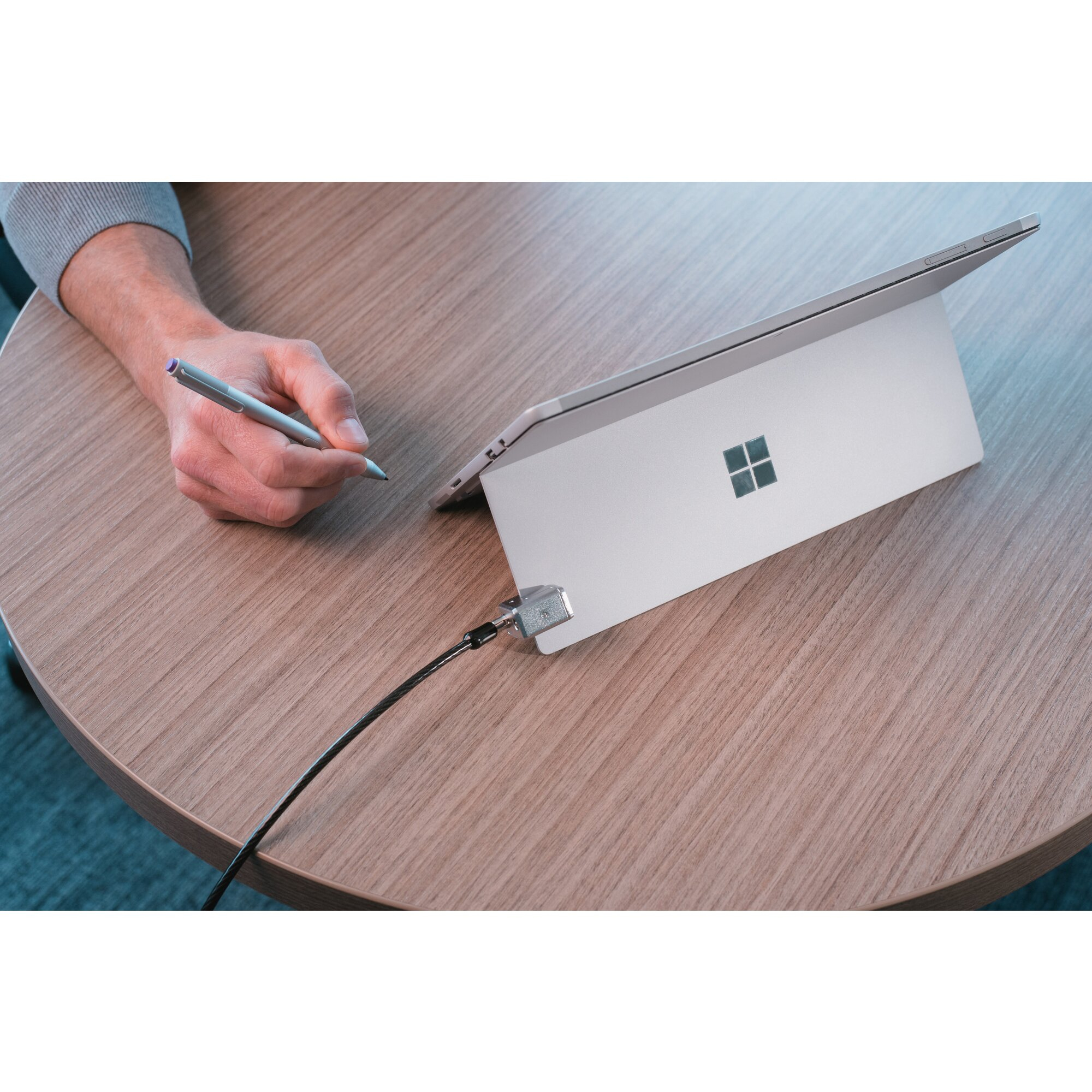 Una mano che tiene uno stilo vicino a un tablet su un tavolo di legno. Un lucchetto di sicurezza è attaccato al tablet.