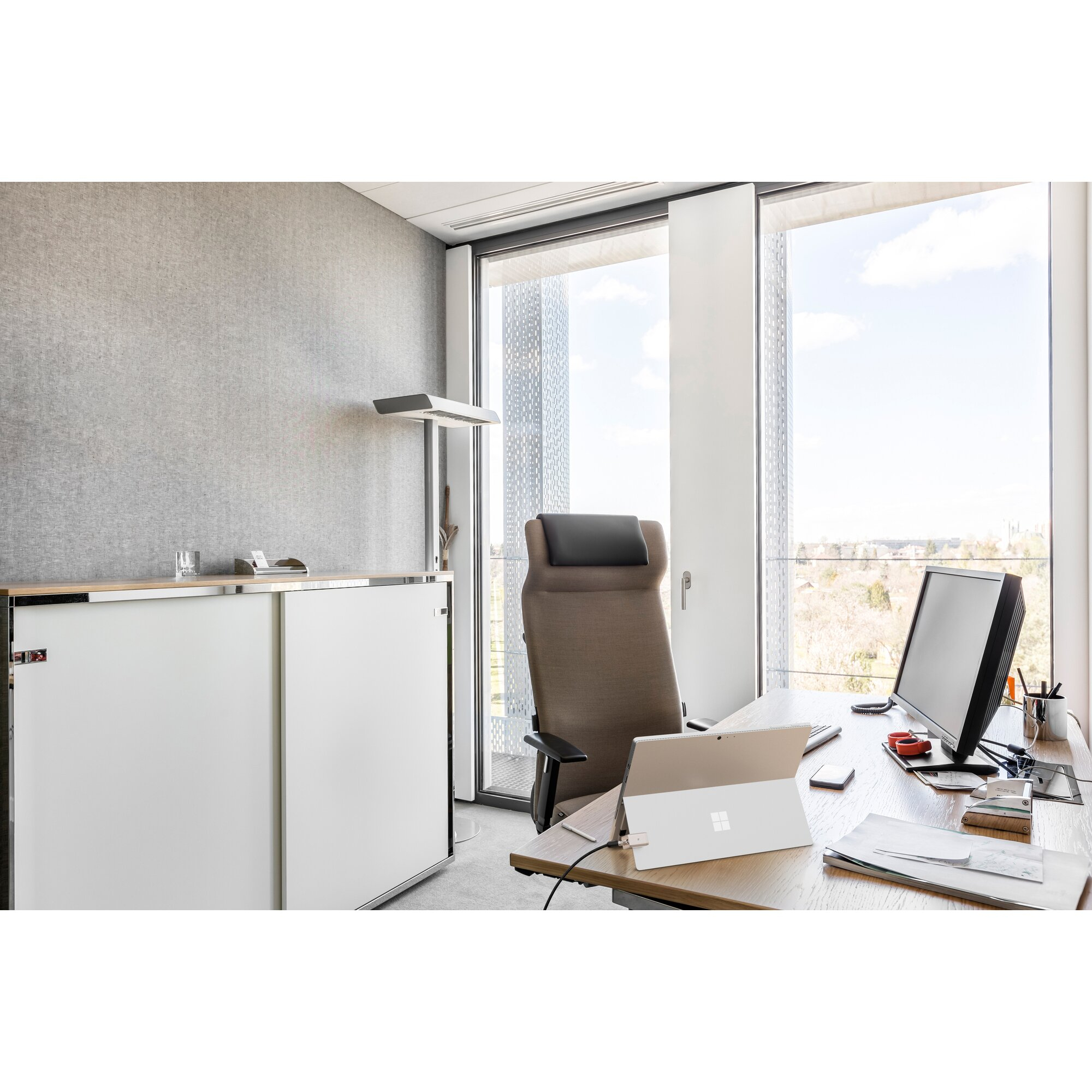 Ufficio con scrivania, computer, sedia e finestra con vista sul paesaggio urbano. Un laptop è sulla scrivania.