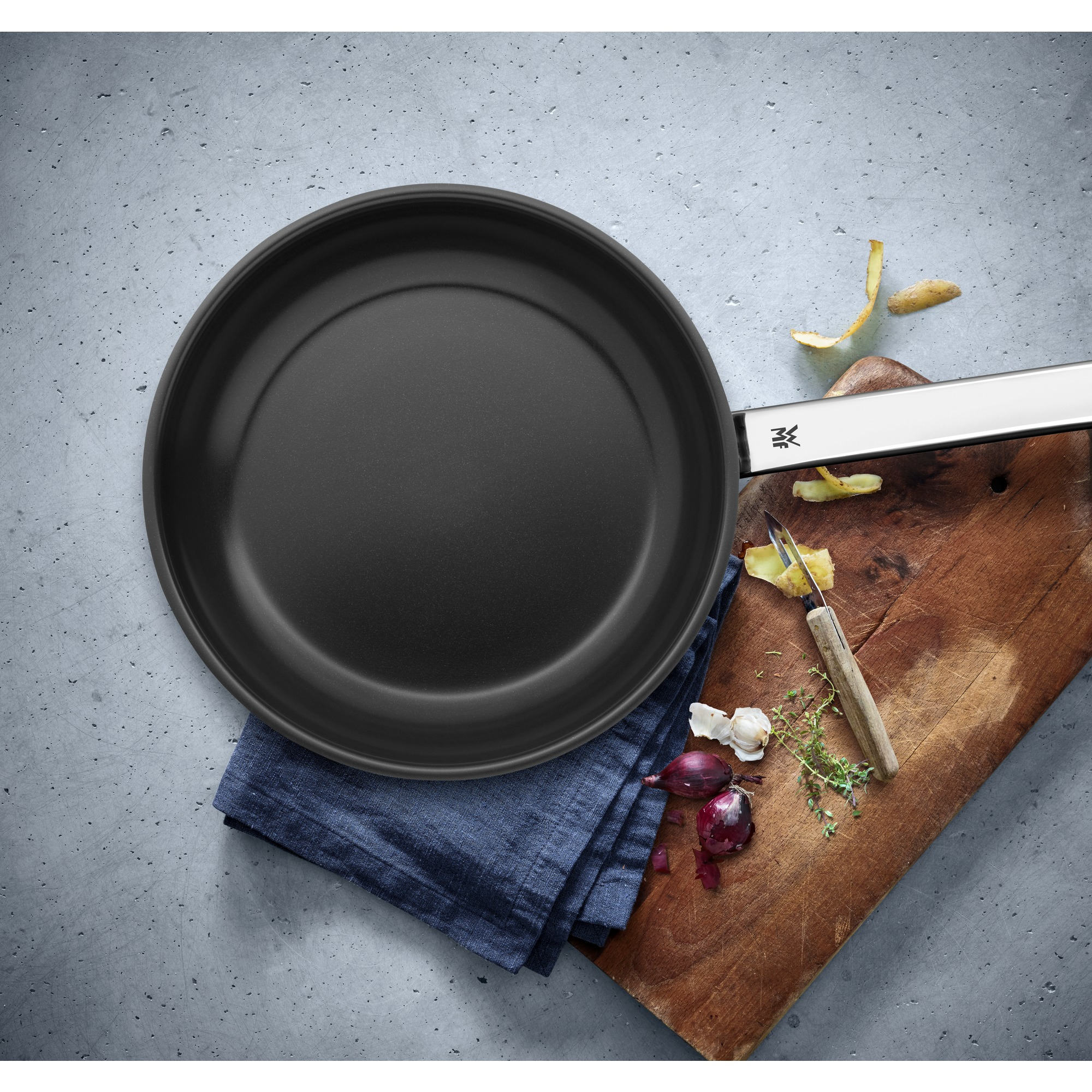 Une poêle noire sur béton avec des ingrédients comme des oignons, des herbes et des pelures de pommes de terre.