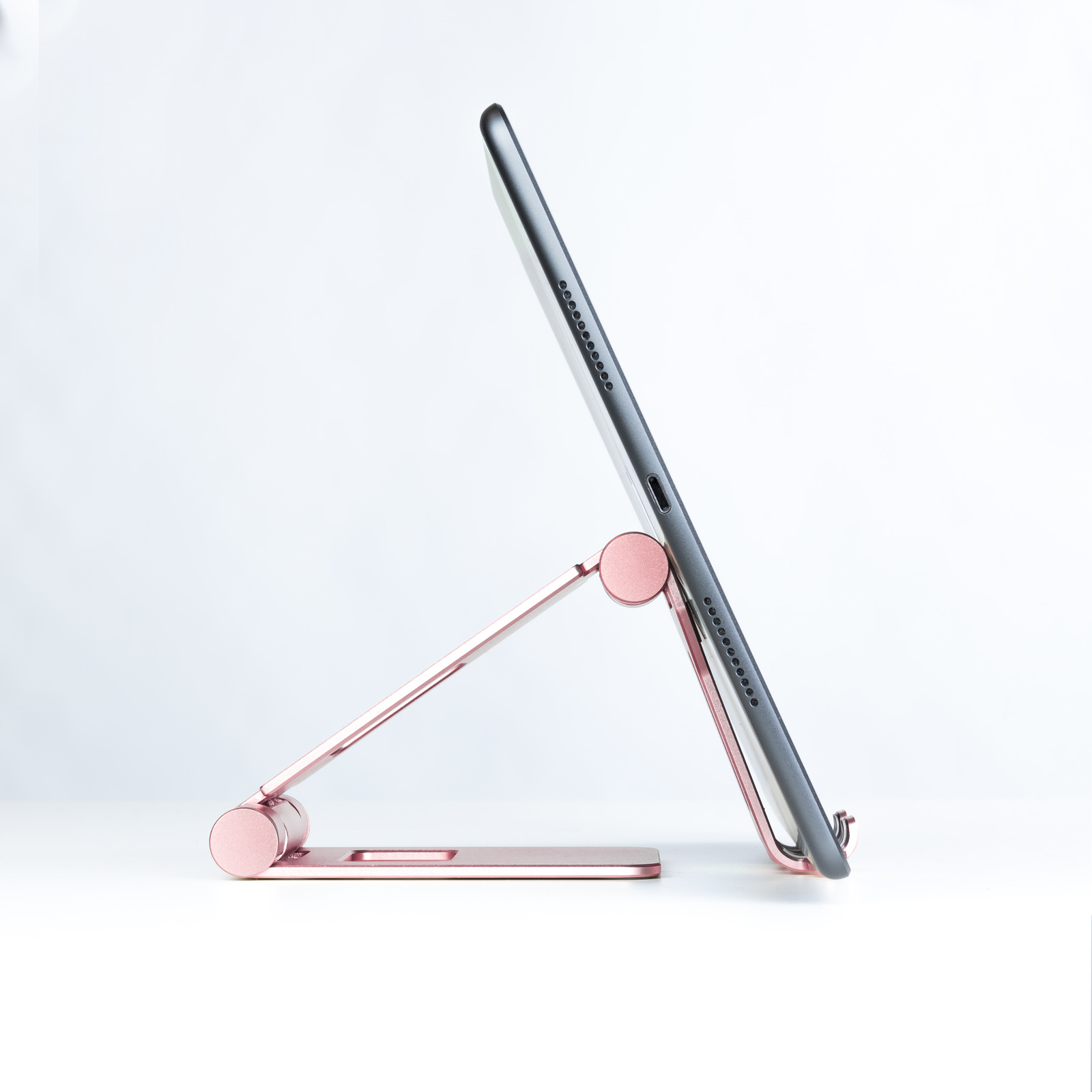 Una tableta está apoyada en un soporte de oro rosa contra un fondo blanco. La tableta es negra.