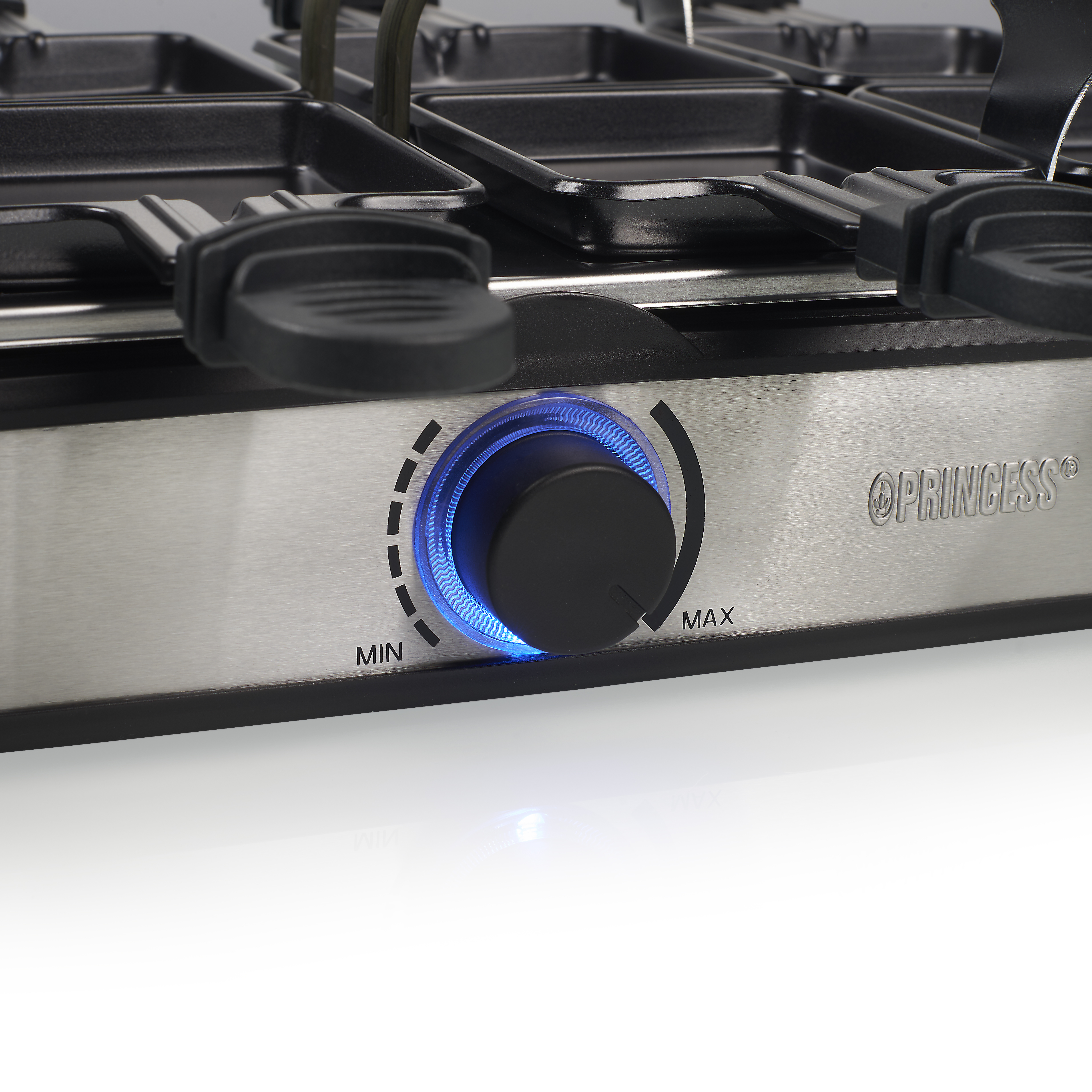 Zbliżenie grilla do raclette. Ma pokrętło z niebieskim światłem i kilka czarnych tacek.