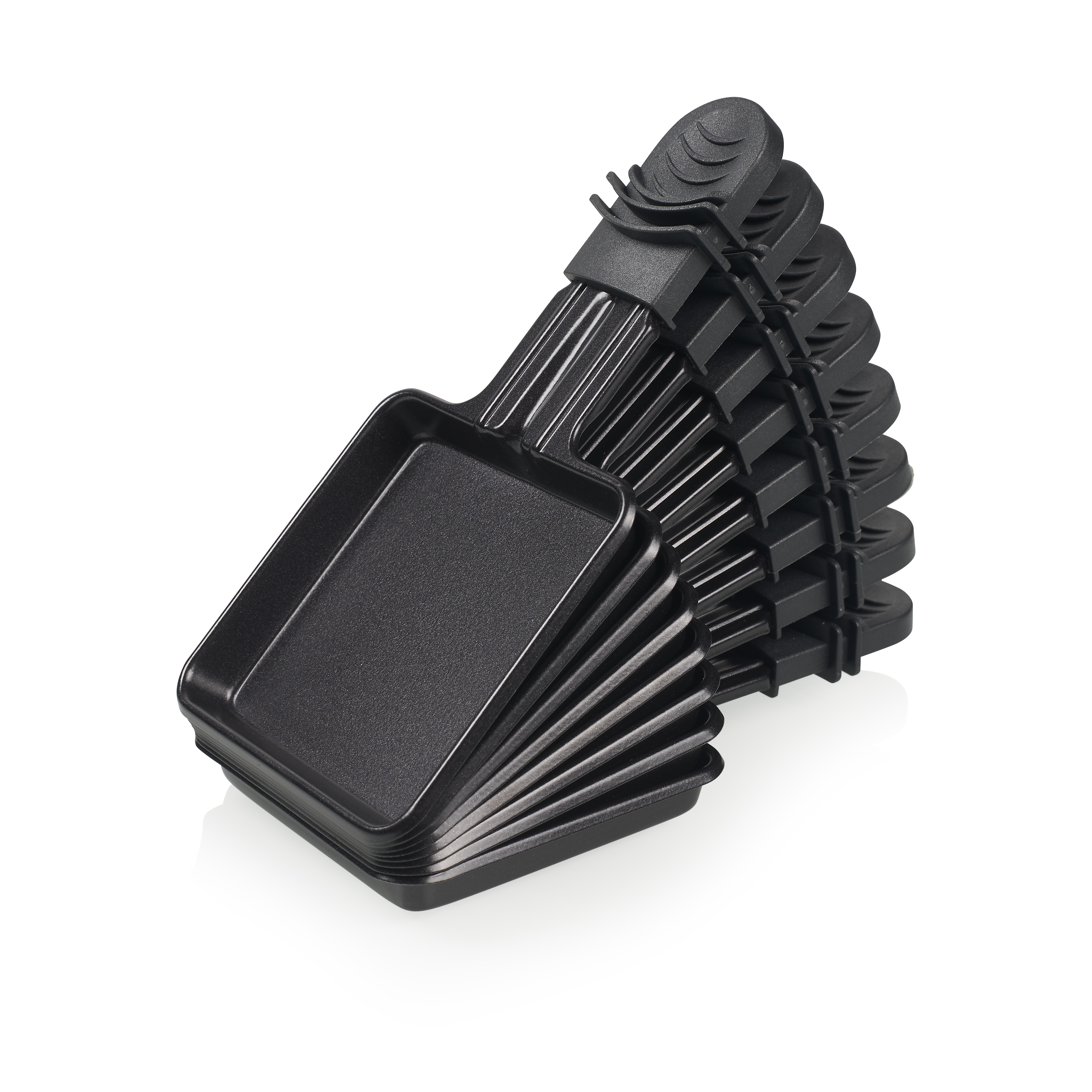 Stos czarnych patelni do grillowania raclette jest wachlarzowato rozłożony na białym tle. Mają uchwyty i są nowe.