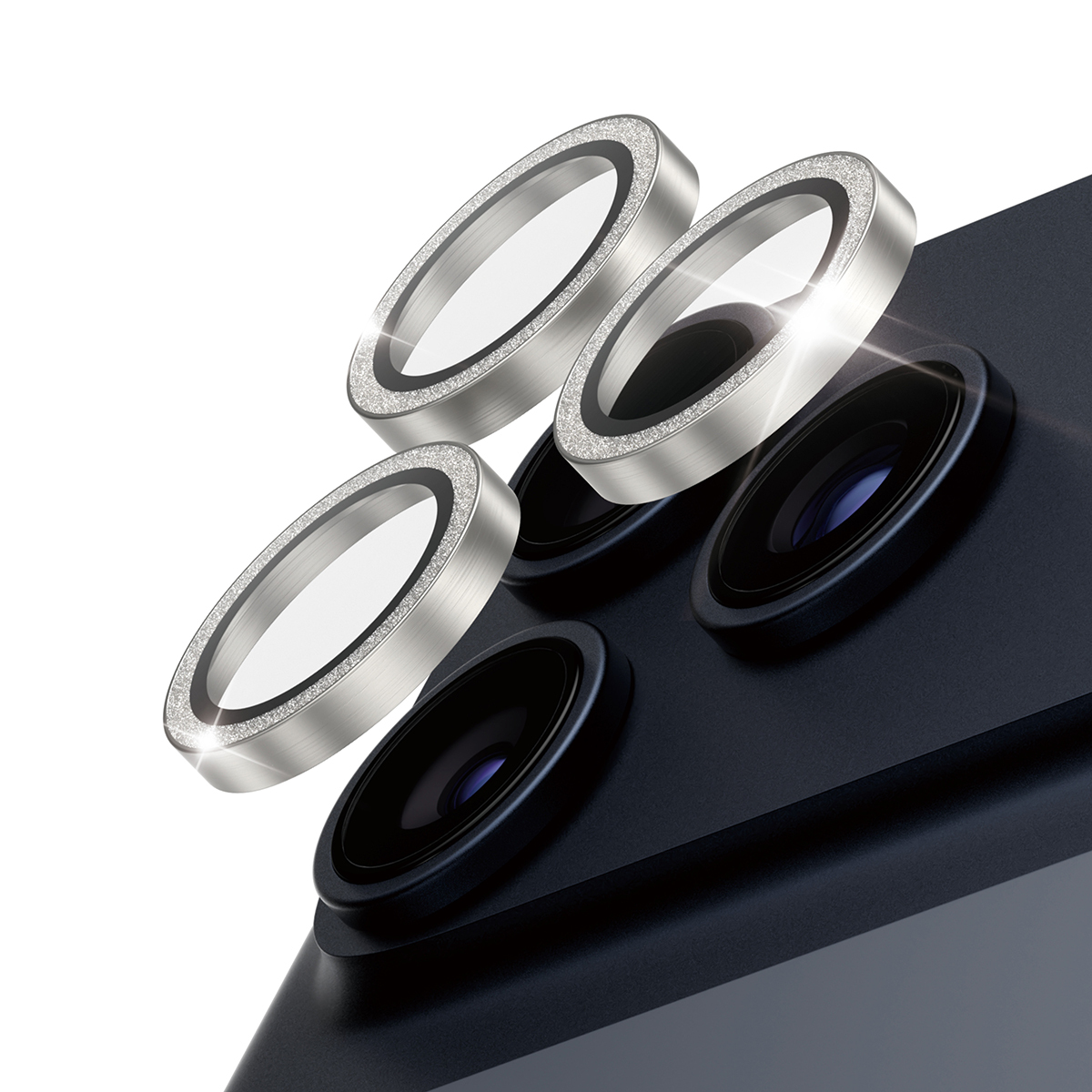 Afbeelding toont lensbeschermers voor telefooncamera's. Zilveren ringen met helder glas en een diamantachtige rand. Donkerblauwe telefoon op de achtergrond.