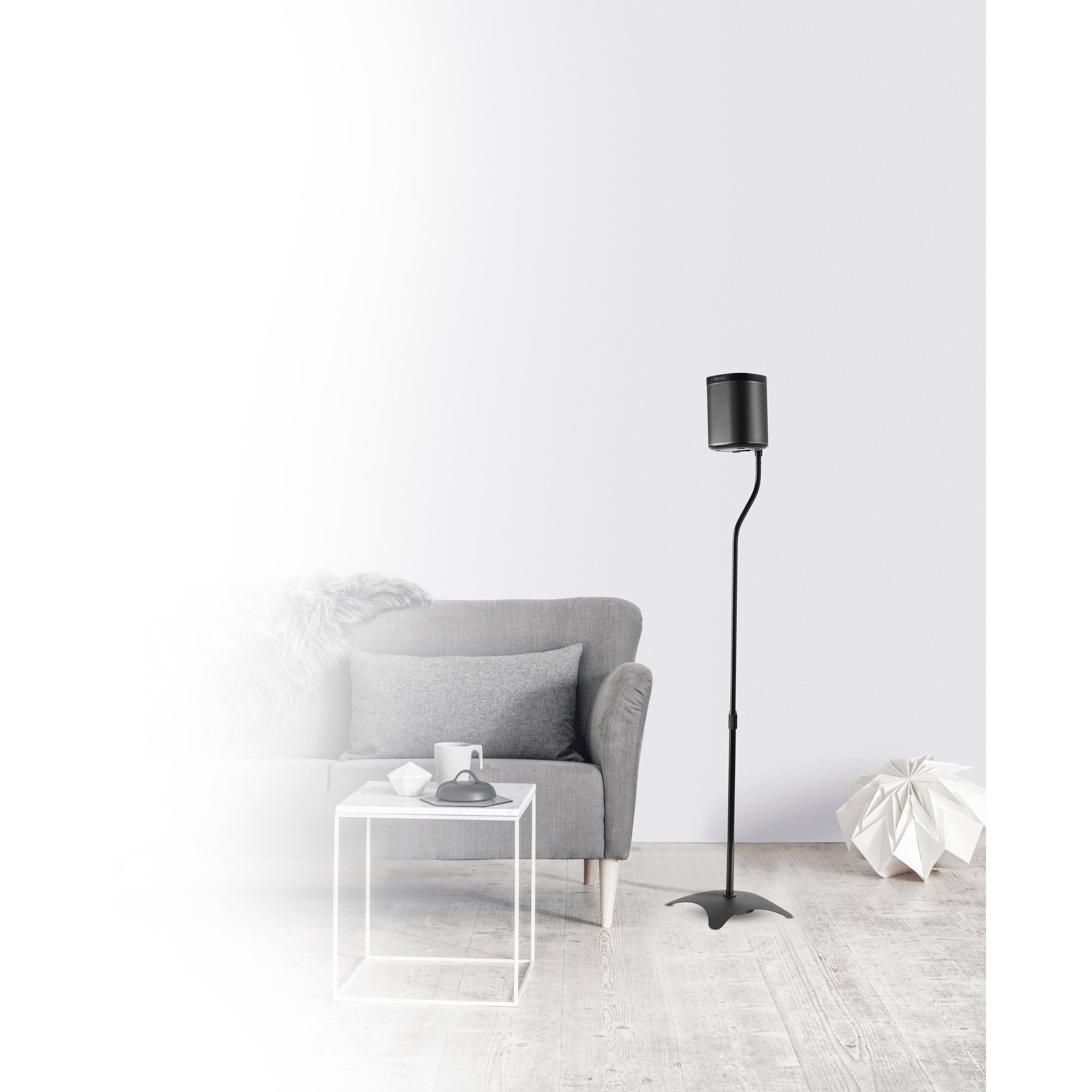 Grauer Sessel, Tisch mit Gegenständen, Lautsprecher auf Ständer und Papierkunst vor weißer Wand und Holzboden.
