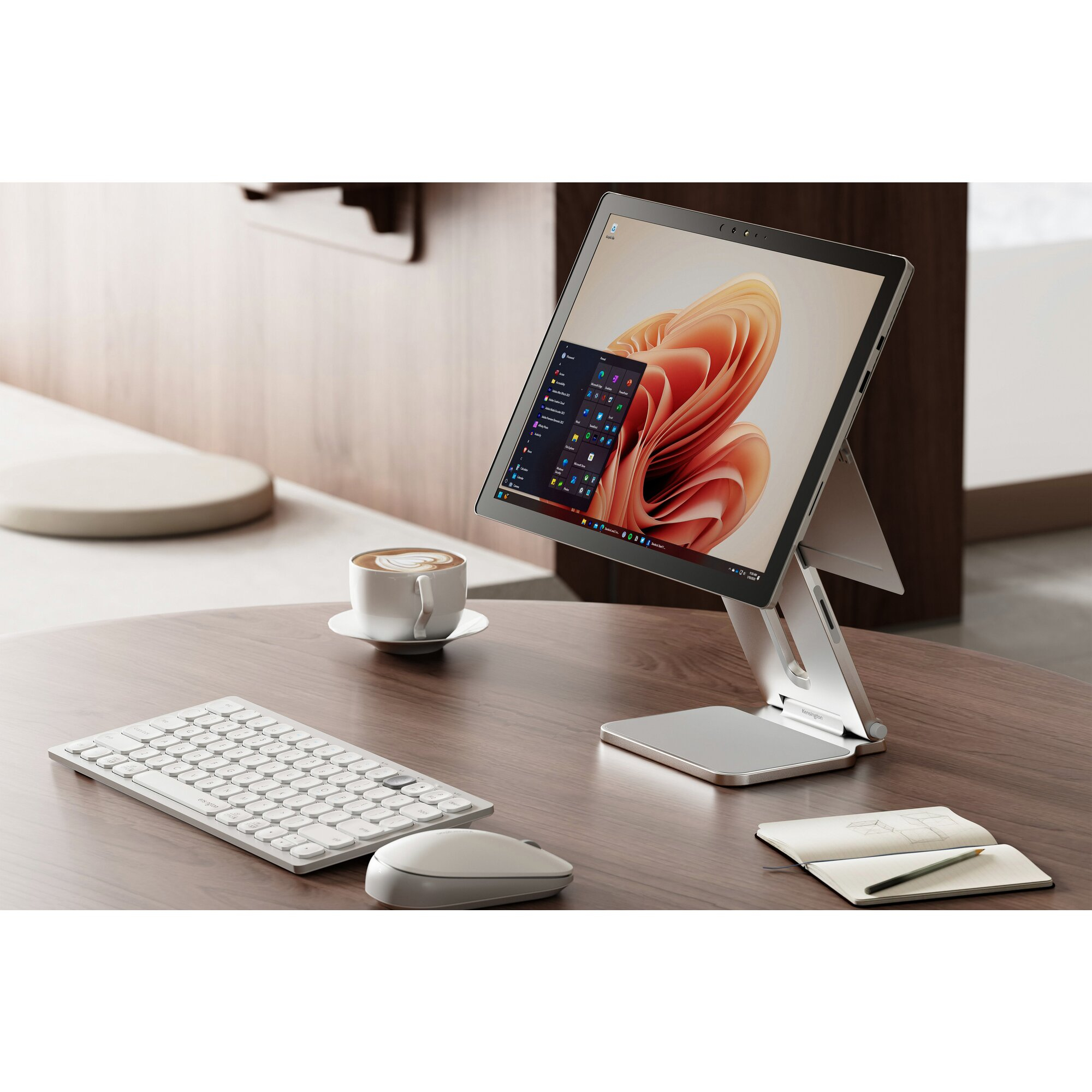 Tablette sur support, clavier, souris, café et bloc-notes sur une table en bois. La tablette affiche un écran coloré.