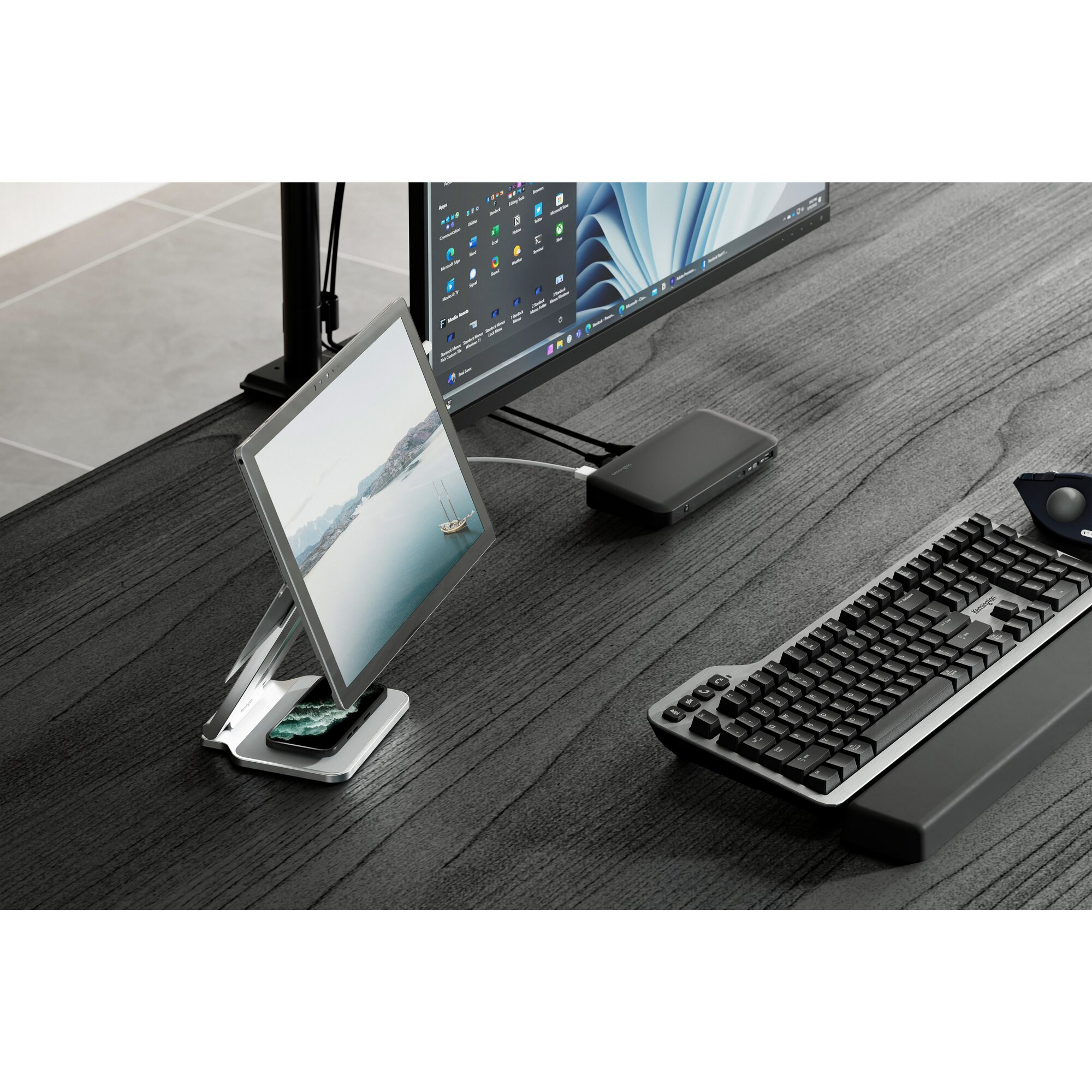 Configuration de bureau avec moniteur, tablette, clavier, souris et station d'accueil. Le bureau est en bois sombre.