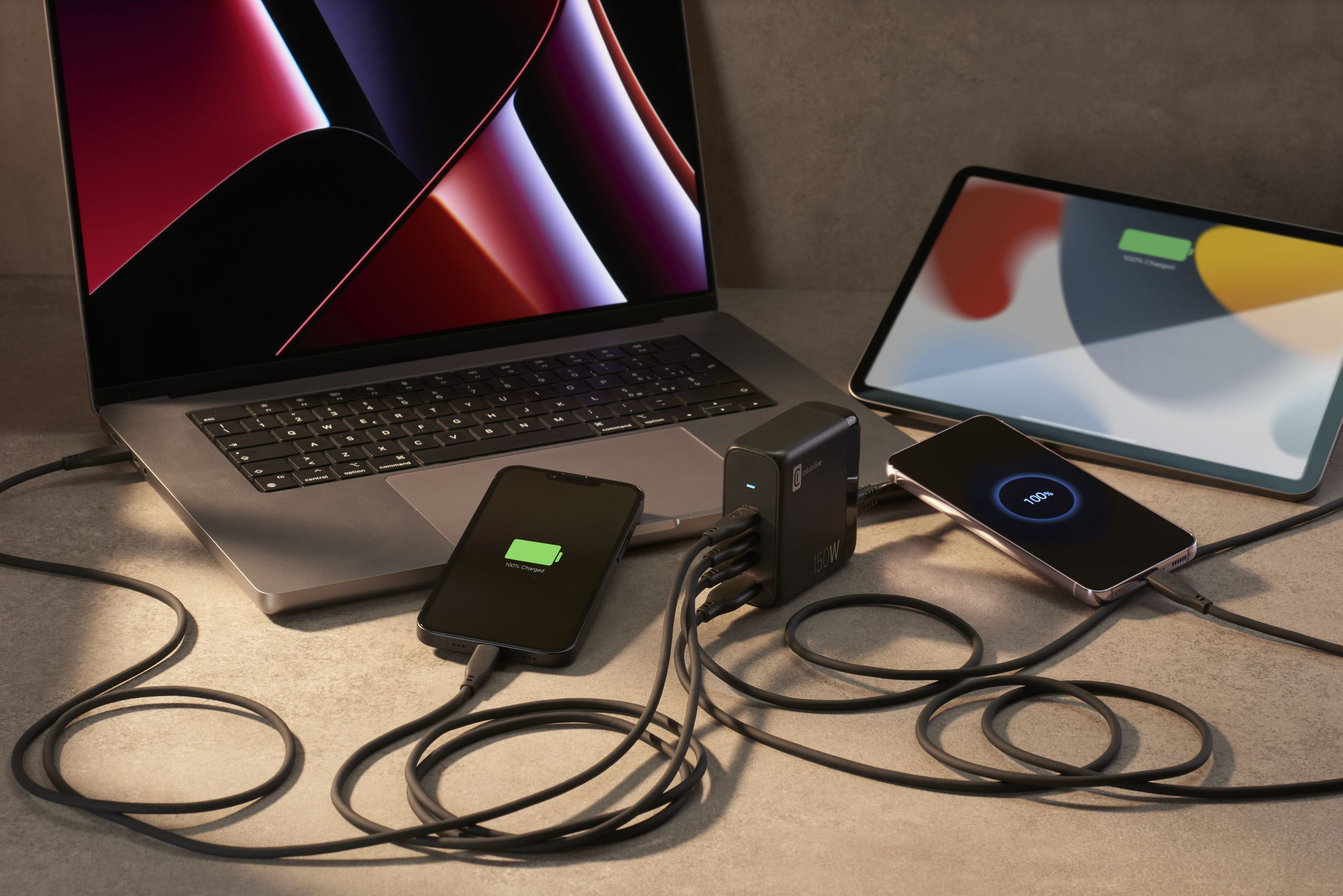 Laptop, Tablet und zwei Telefone werden über einen Netzadapter aufgeladen. Alle Geräte zeigen Ladestatus.