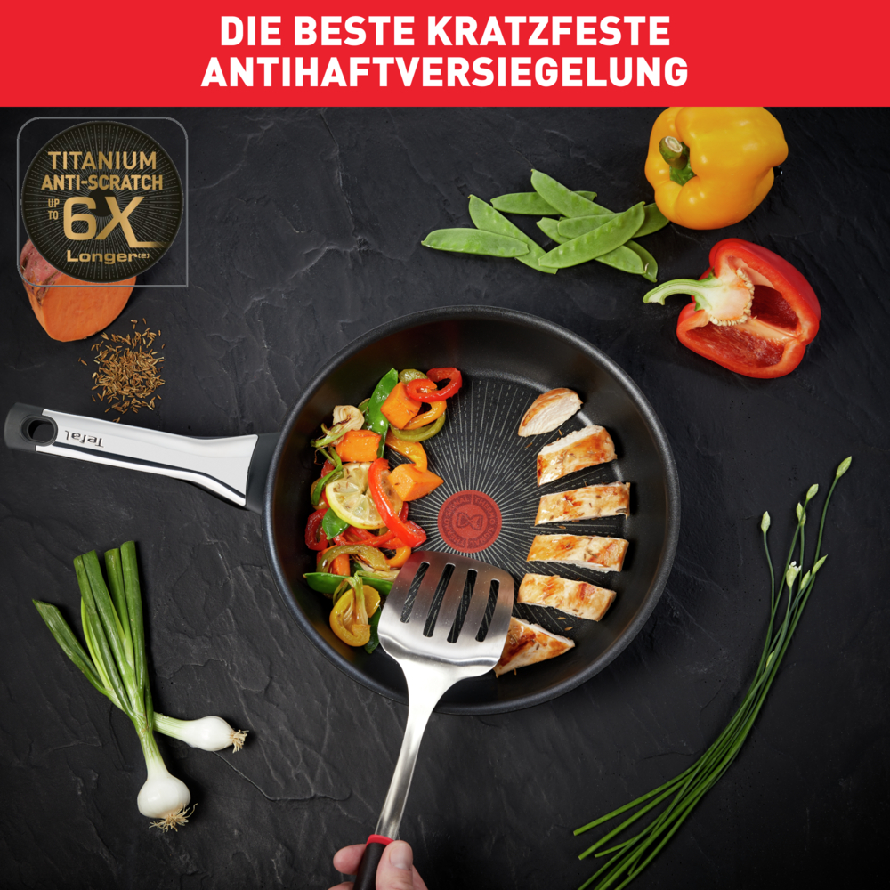 Patelnia z warzywami i kurczakiem. Obecne są również żółte i czerwone papryki, fasolka szparagowa i cebula. Patelnia stoi na czarnej powierzchni.