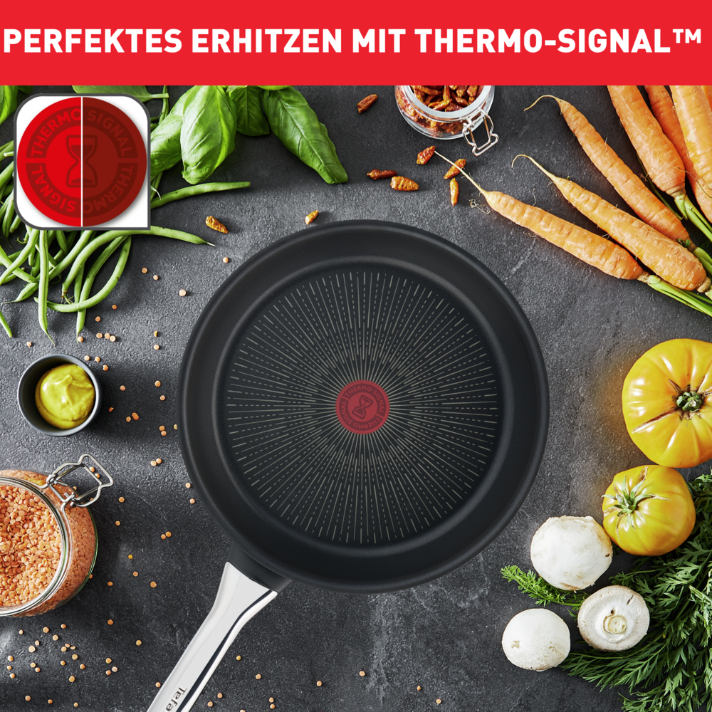 Czarna patelnia z warzywami wokół. Widoczne są marchewki, pomidory, grzyby, bazylia i słoik z soczewicą.