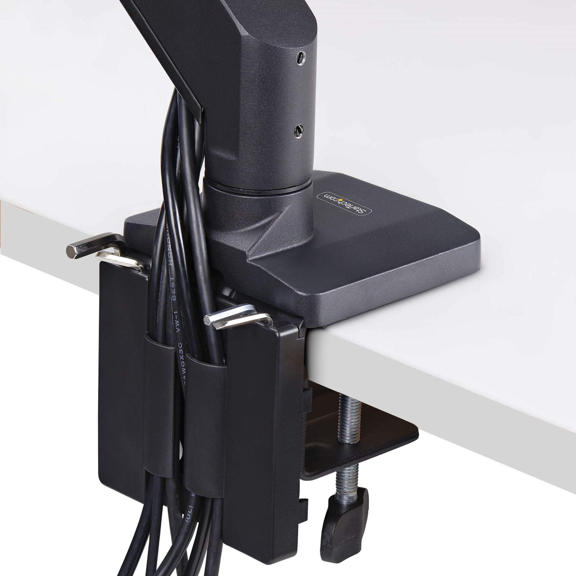Schwarzer Monitorarm wird an einem weißen Schreibtisch befestigt. Kabel werden von einem schwarzen Halter gehalten.