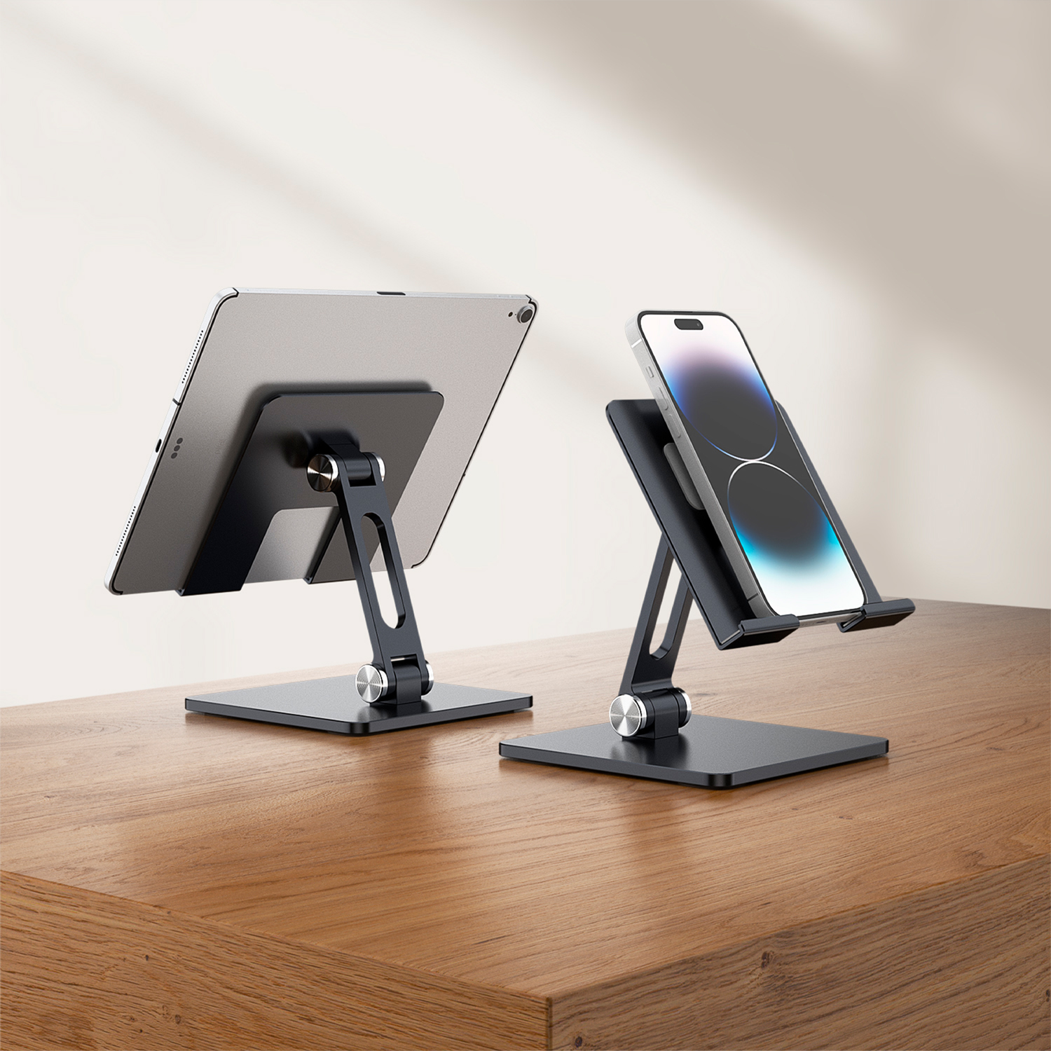 Zwei schwarze Telefonständer, die ein Tablet und ein Smartphone halten, auf einem Holztisch platziert. Hintergrund ist eine helle Wand.