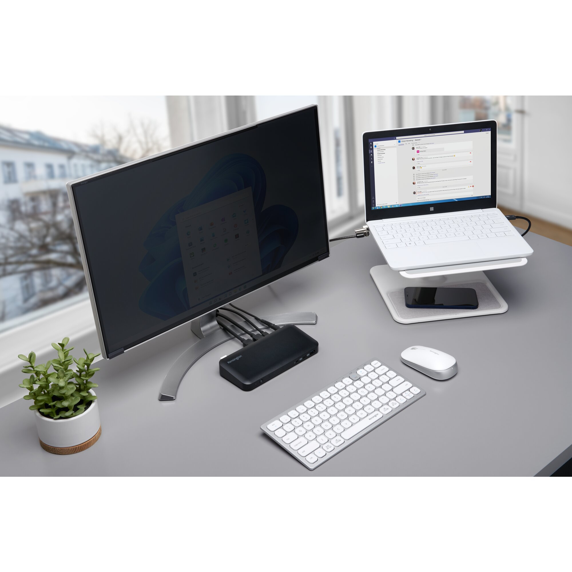 Una configuración de escritorio con monitor, portátil, teclado, ratón y una planta. Escritorio de Windows en ambas pantallas.