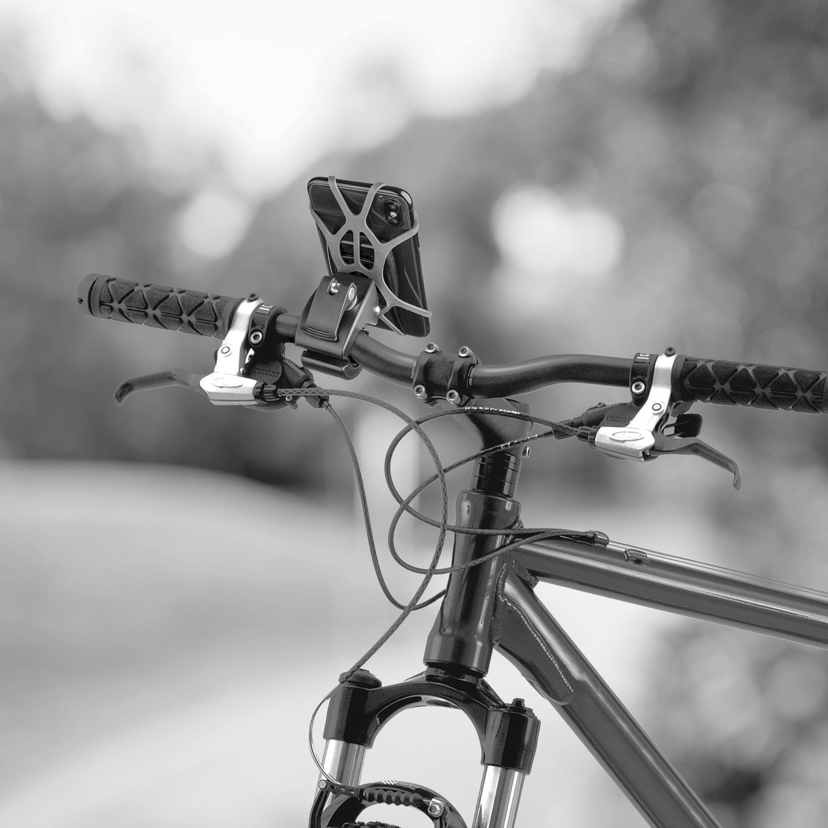 Manillar de bicicleta con soporte para teléfono. Se ven las manetas de freno, los puños texturizados y los cables. Fondo borroso.