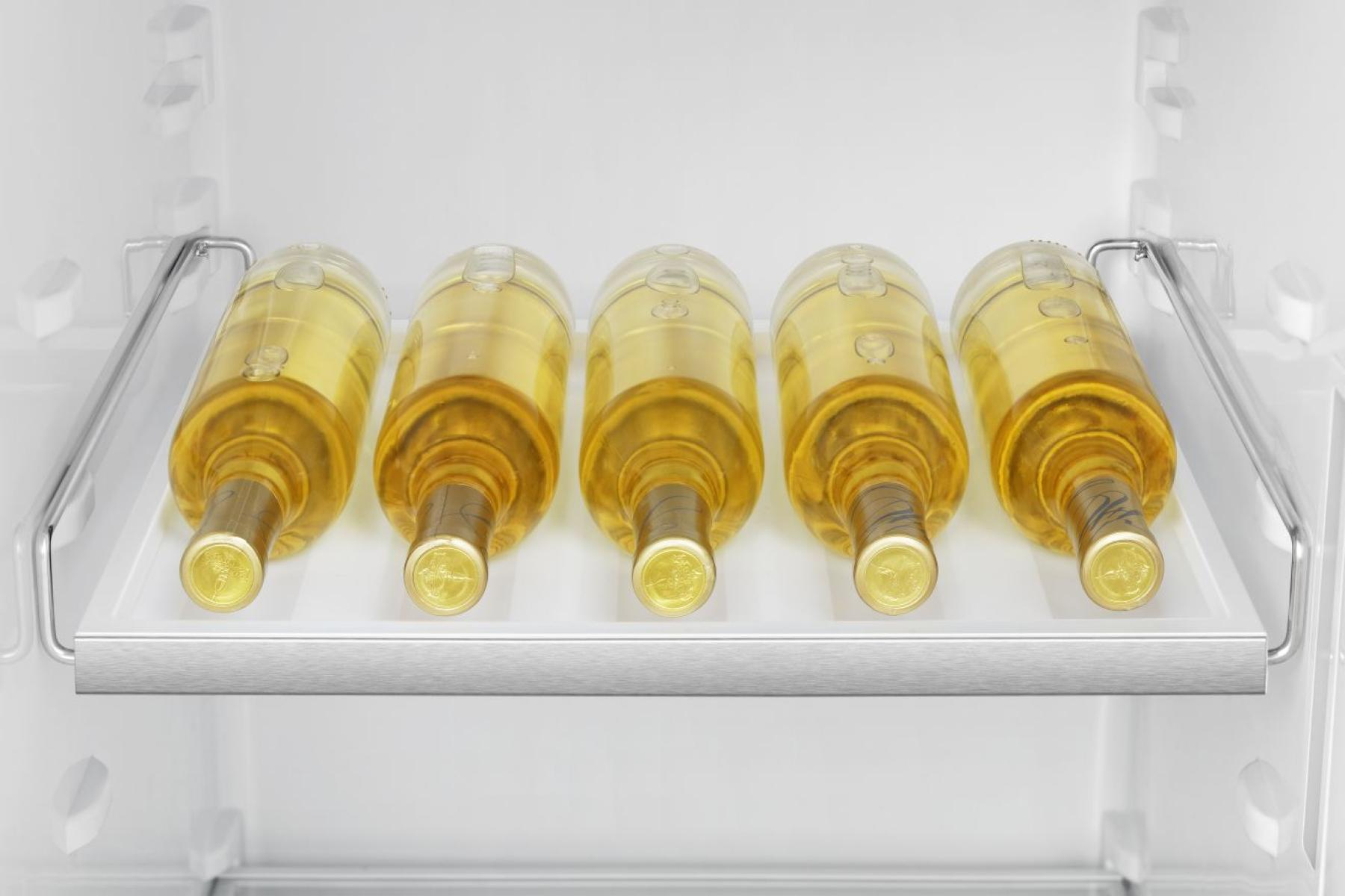 Cinque bottiglie di vino in un frigorifero. Sono su uno scaffale. Le bottiglie sono piene di liquido giallo e hanno etichette dorate.
