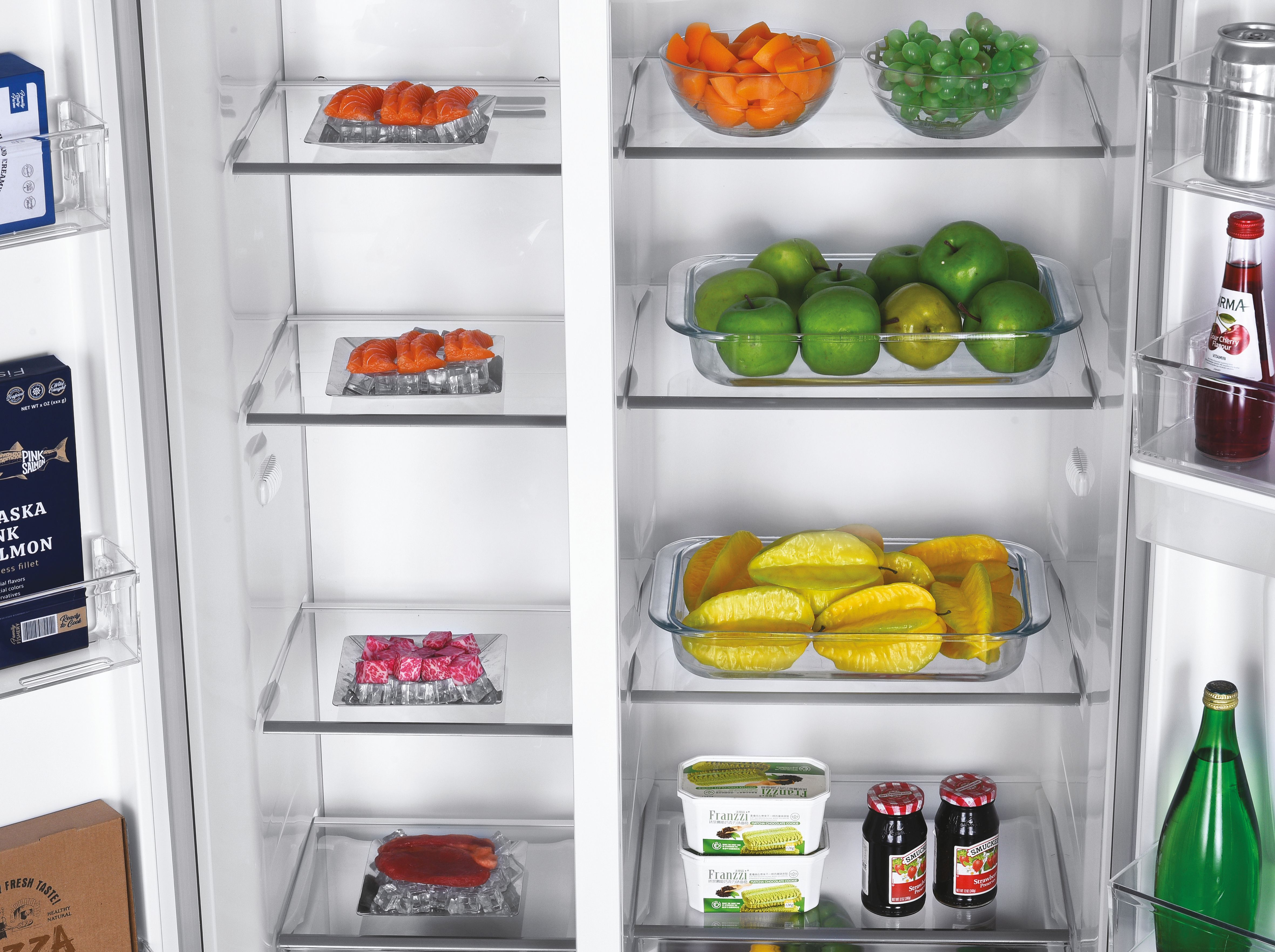 Un refrigerador abierto muestra salmón, fruta y bocadillos en los estantes. Zanahorias, uvas, manzanas y carambolas.