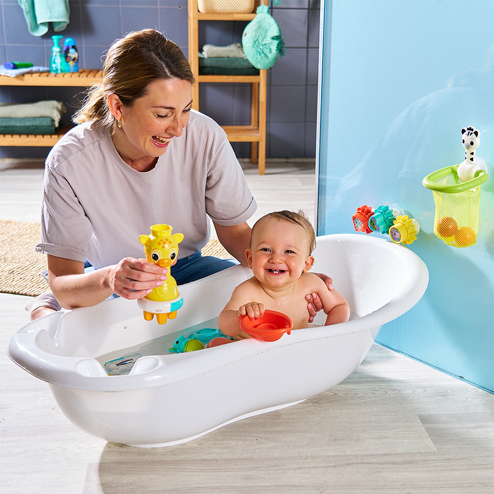 Eine Frau und ein Baby befinden sich mit Spielzeug in einer Badewanne. Das Baby lächelt. Die Frau hält ein Giraffenspielzeug.
