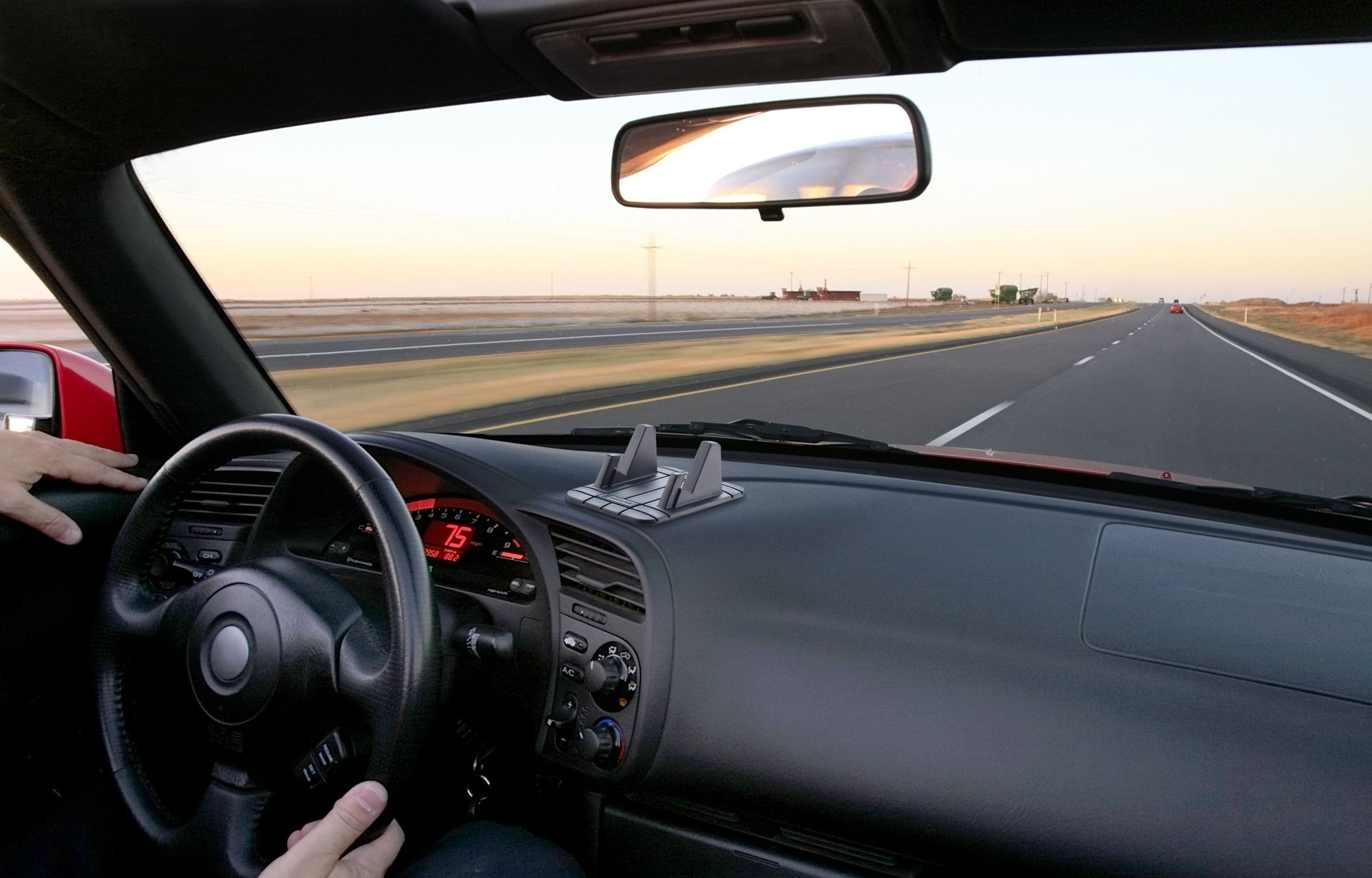 Blick aus dem Auto auf eine Autobahn im Sonnenuntergang. Lenkrad, Armaturenbrett und eine Straße voraus. Autoinnenraum.