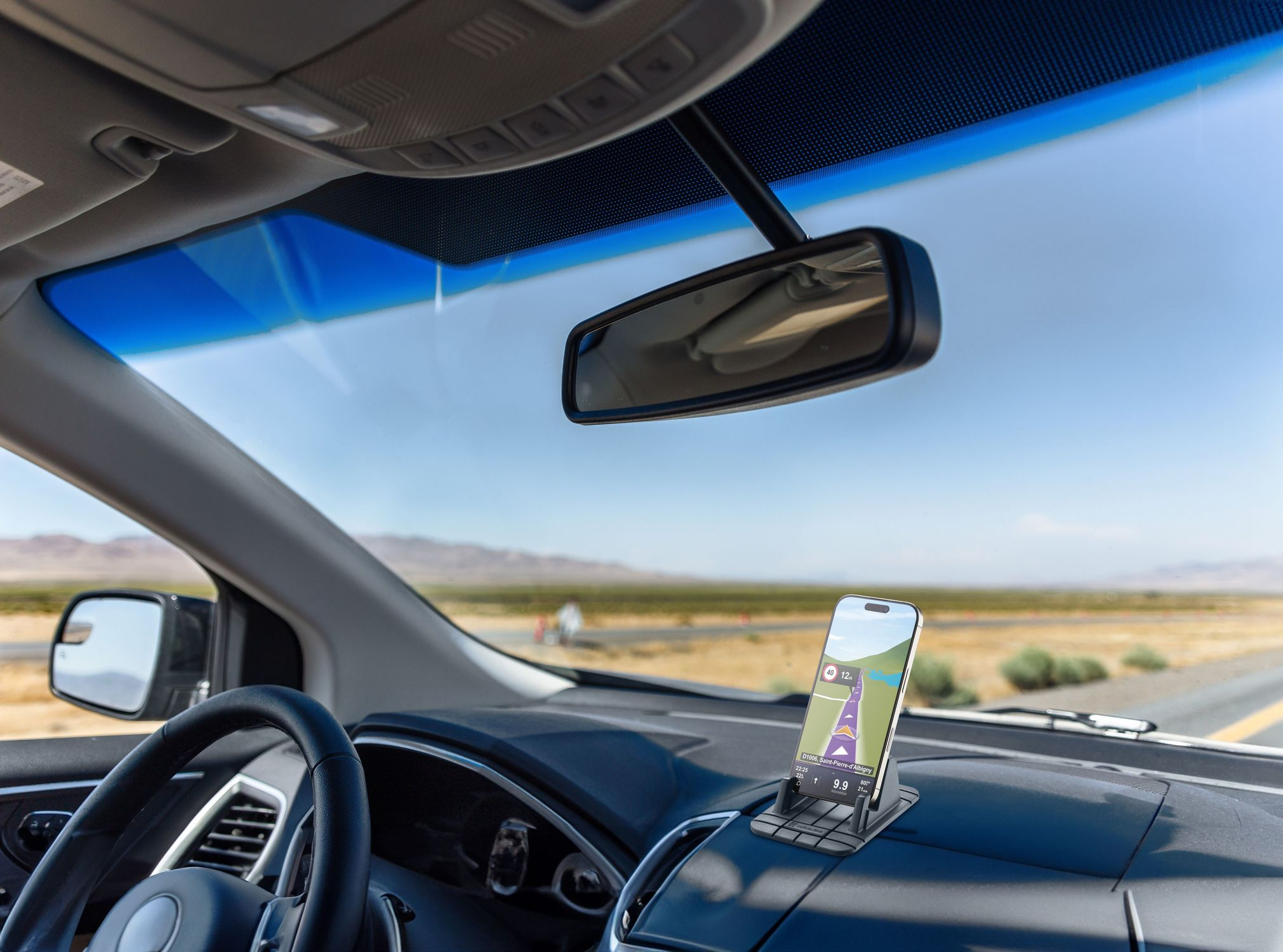 Im Auto, Telefon mit GPS auf dem Armaturenbrett. Lenkrad, Spiegel und Straße durch die Windschutzscheibe sichtbar. Berge im Hintergrund.
