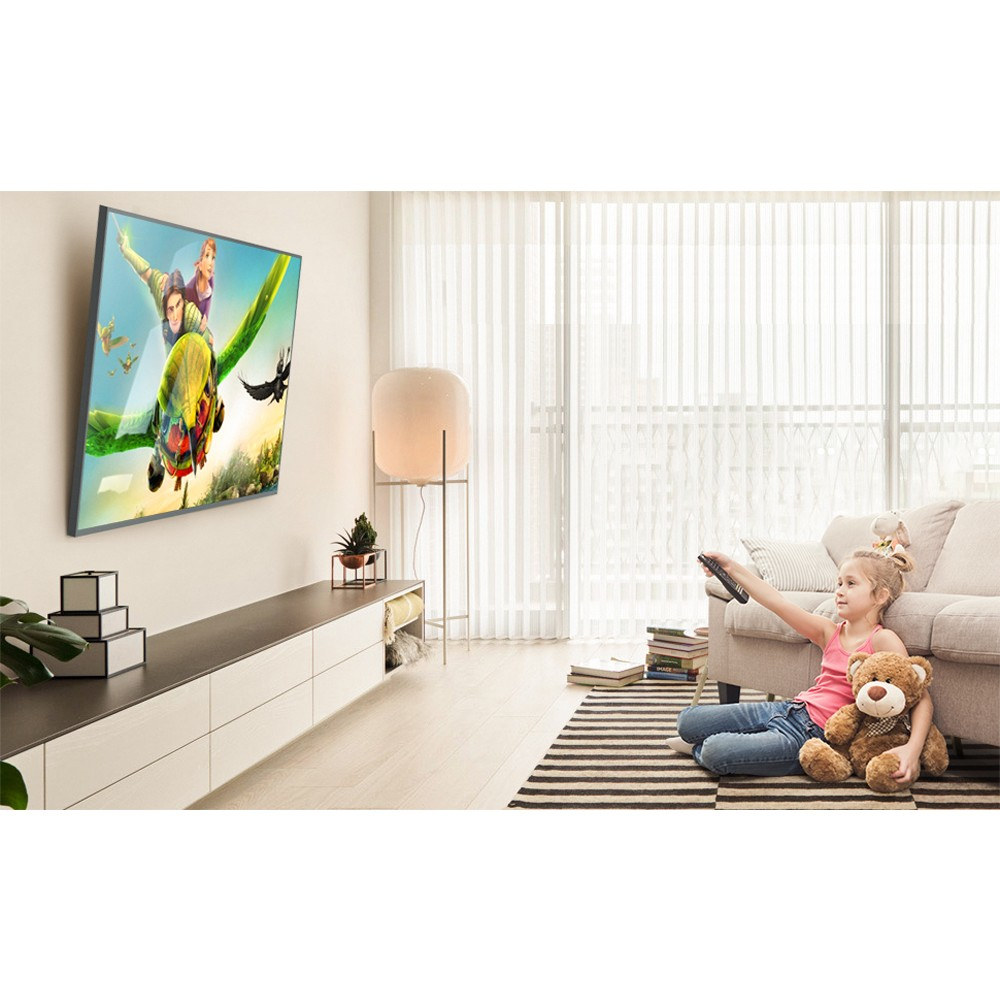 Ein Mädchen sitzt auf einem Teppich und hält eine Fernbedienung. Ein Fernseher zeigt eine Animation. Ein Teddybär ist neben ihr.