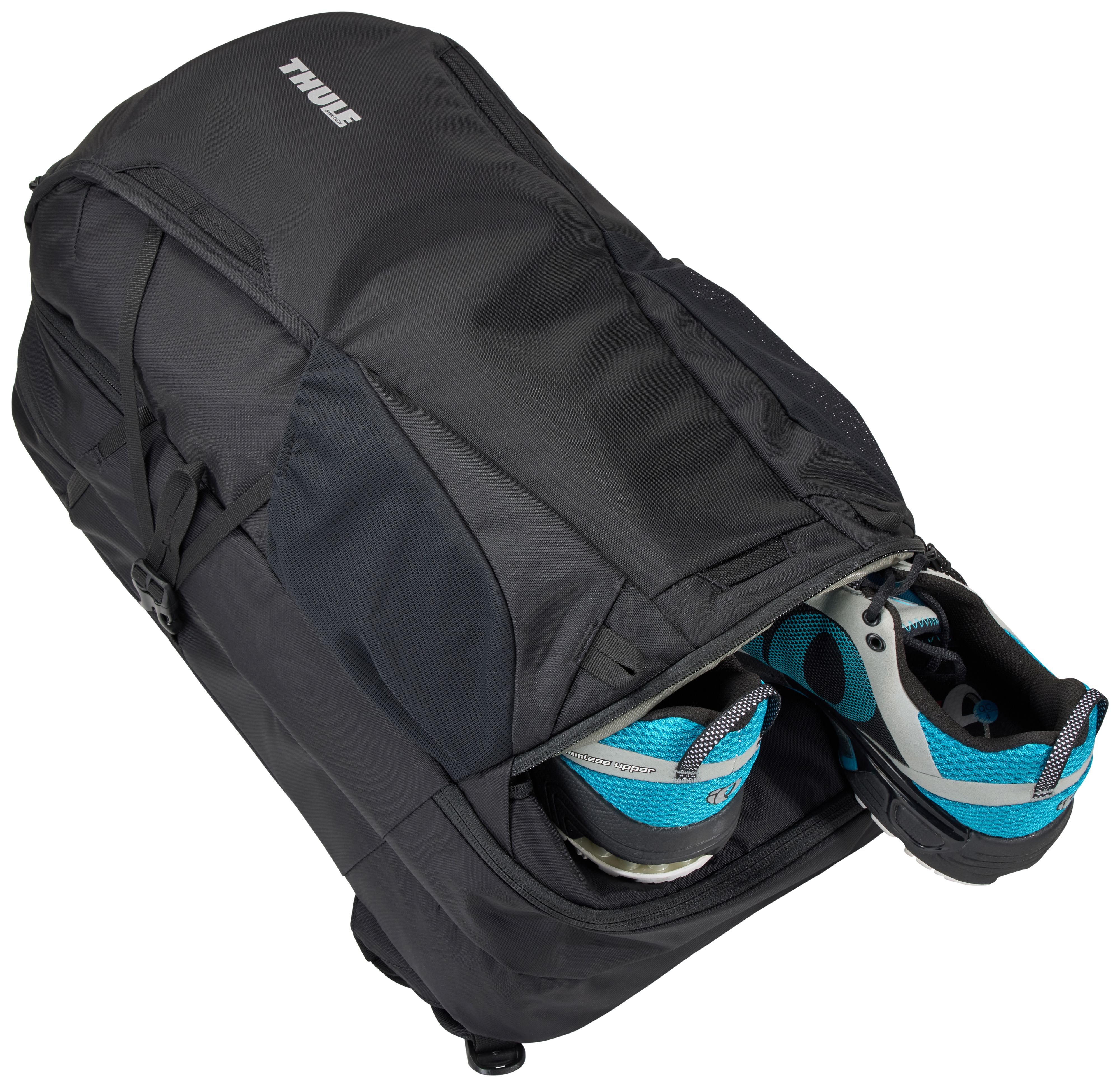 Schwarzer Thule-Rucksack mit blauen und weißen Laufschuhen. Weißer Hintergrund. Der Rucksack ist offen.