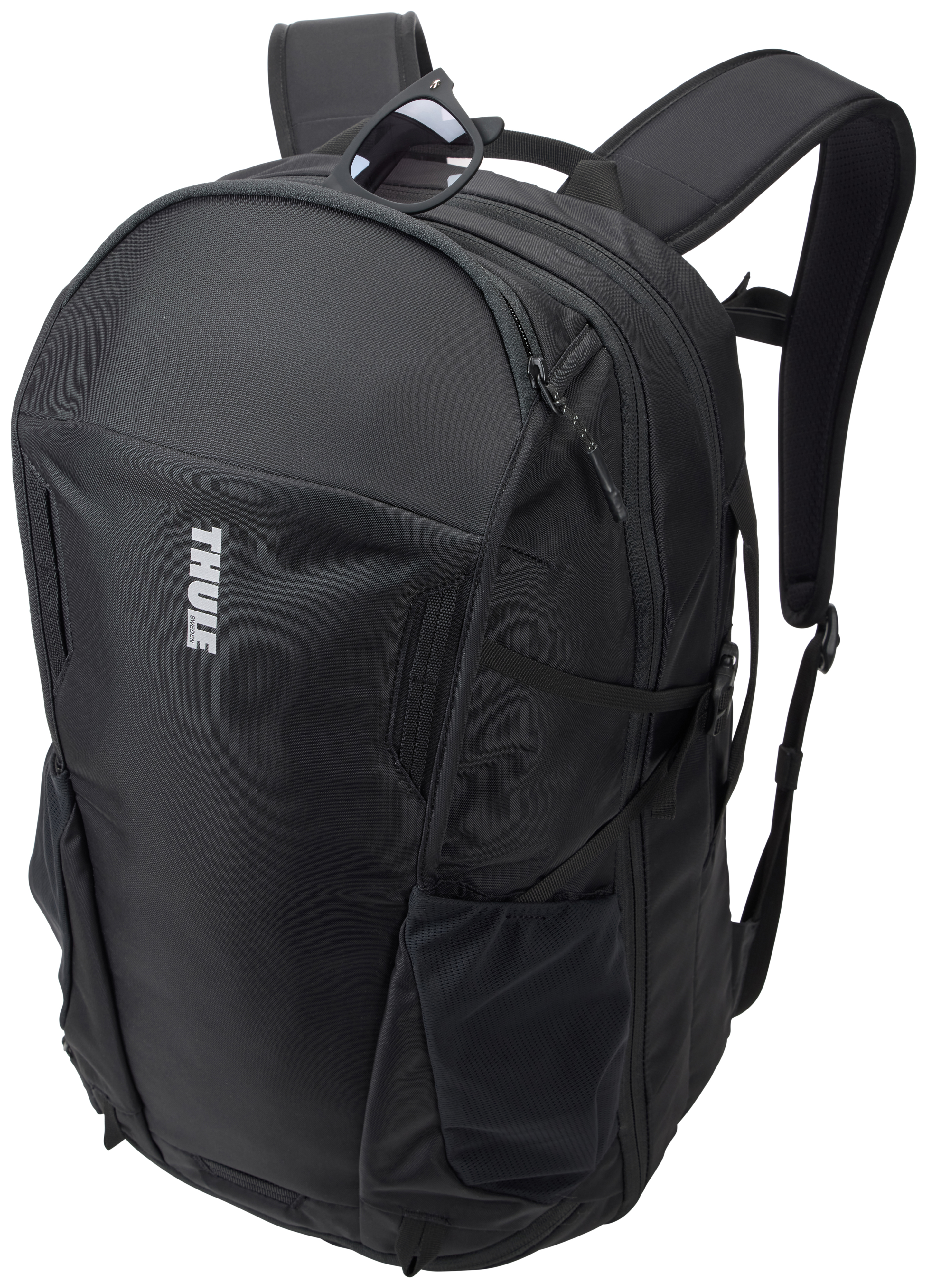 Schwarzer Rucksack mit Sonnenbrille obenauf. Mit Thule-Logo. Hat mehrere Taschen und gepolsterte Gurte. Isoliert auf Weiß.