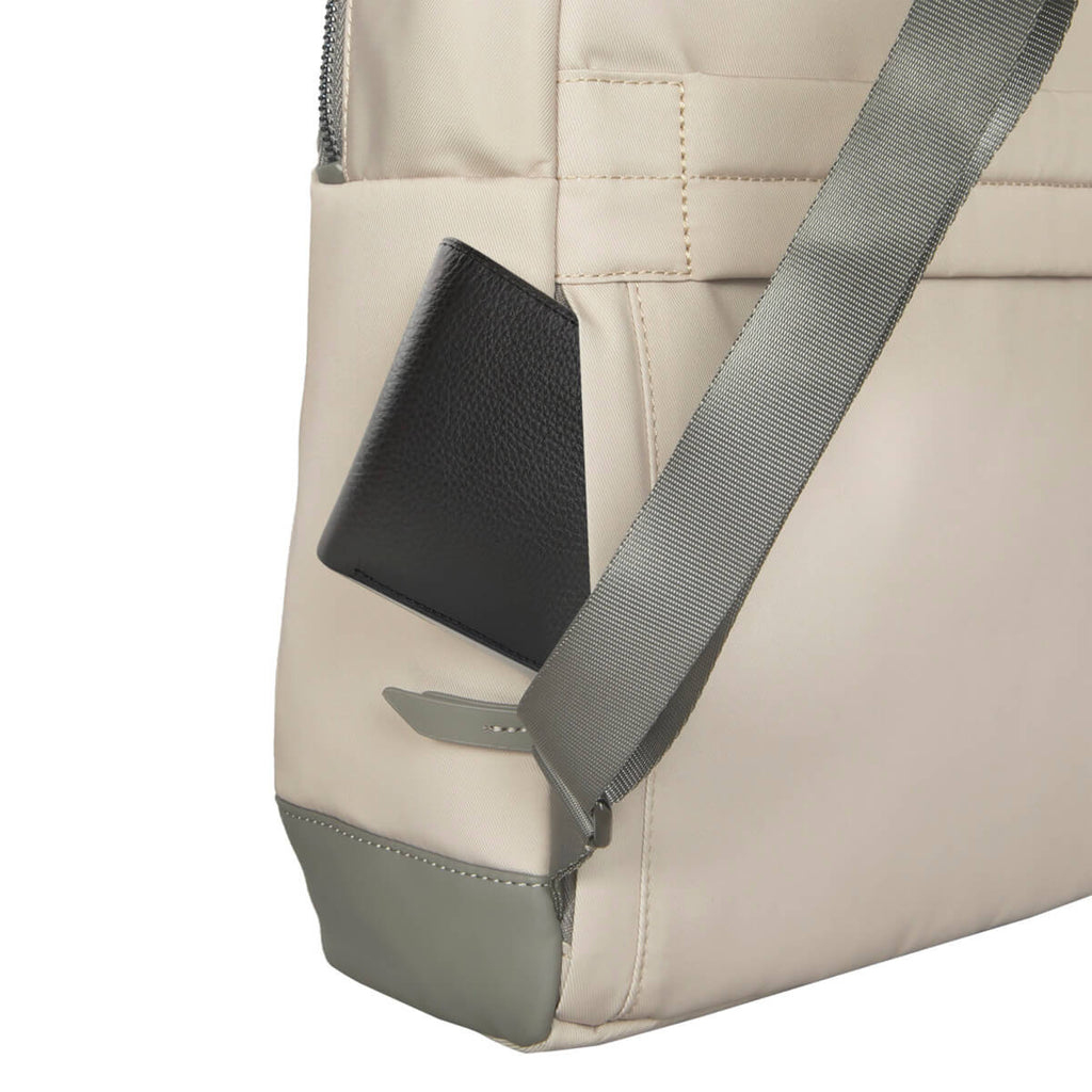 Ein beiger Rucksack mit einer schwarzen Brieftasche in der Seitentasche. Ein grauer Riemen ist sichtbar. Der Boden der Tasche ist grau.