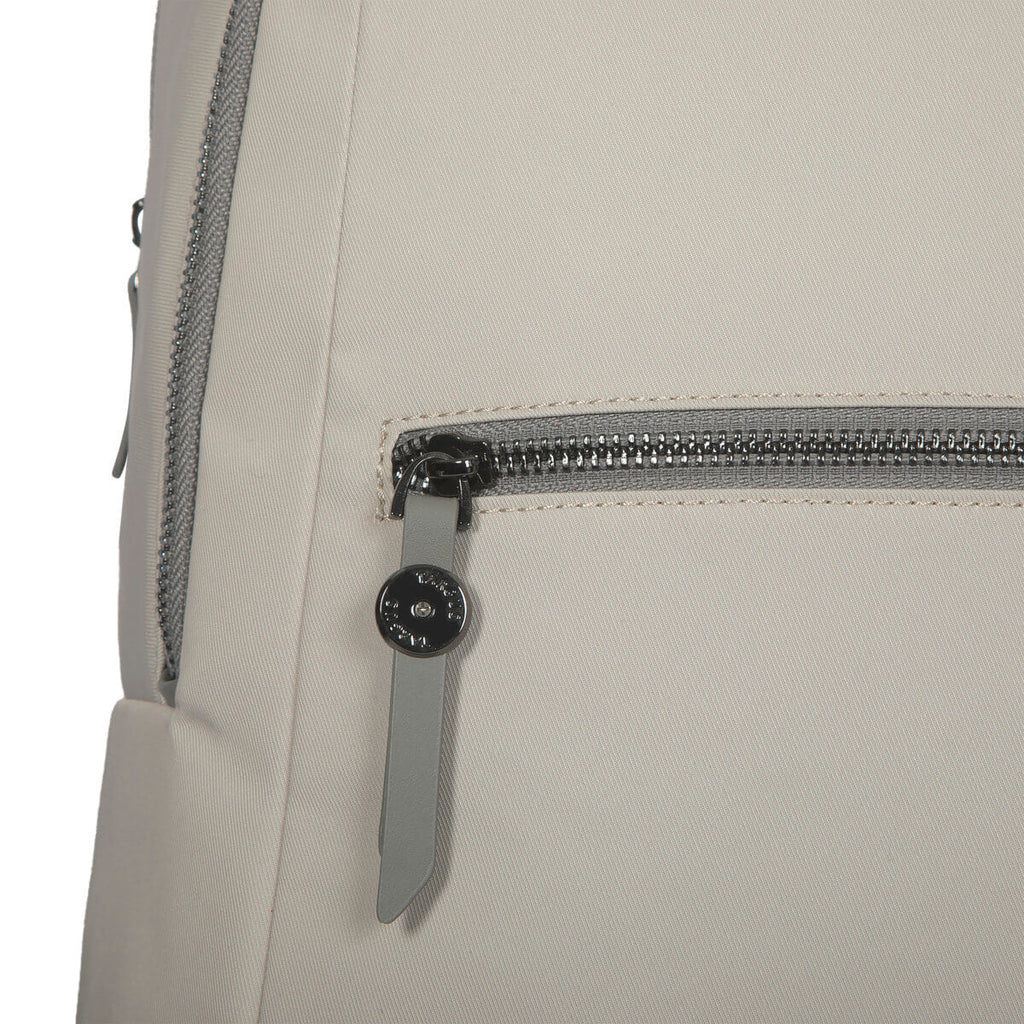 Nahaufnahme einer beigefarbenen Stofftasche mit silbernem Reißverschluss und grauem Leder-Zuglasche. Ein kleiner, runder Metallknopf ist befestigt.