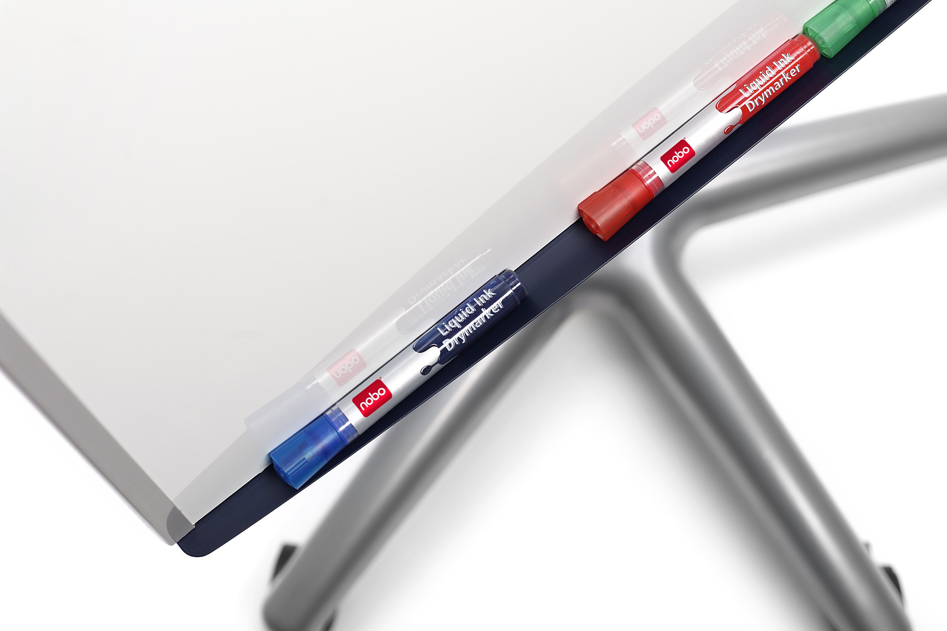 Nahaufnahme eines Whiteboards mit farbigen Markern. Marker sind rot, blau und grün. Ein Metallrahmen ist sichtbar.