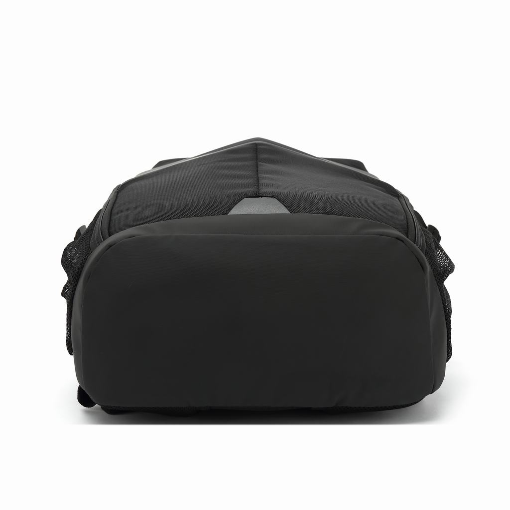 Una mochila negra, vista desde abajo, sobre un fondo blanco. Tiene una base redondeada y un parche reflectante en la parte superior.