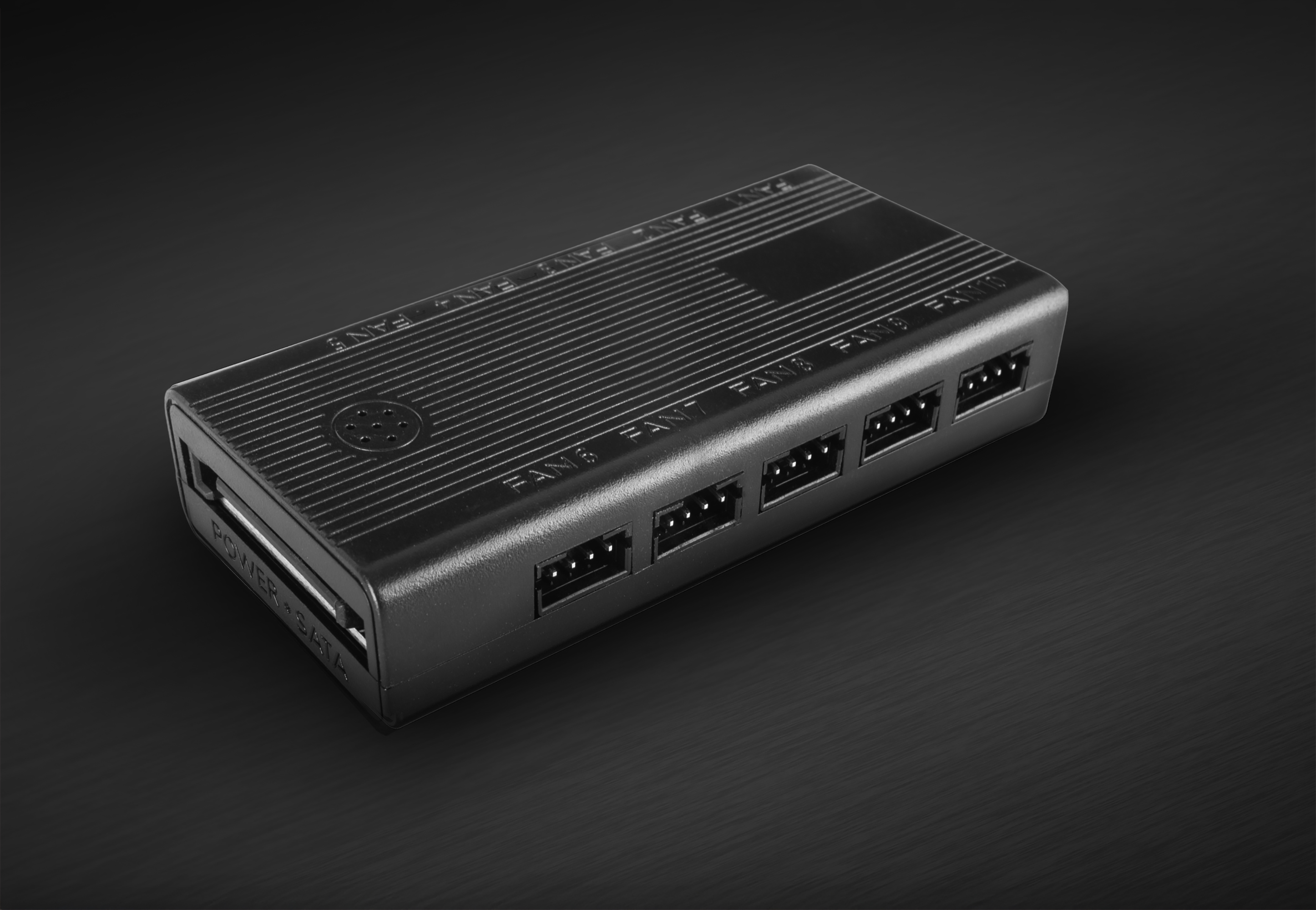 Controlador de ventilador negro con múltiples conectores, etiquetado 'FANS' sobre una superficie oscura.