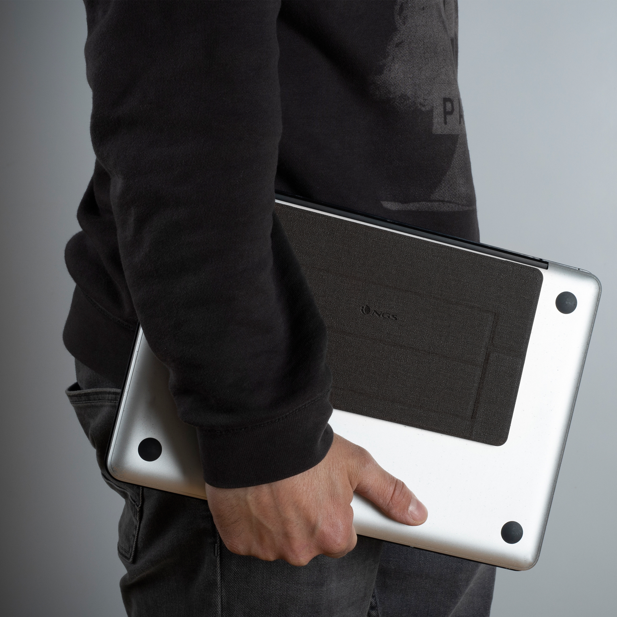 Person hält einen silbernen Laptop mit schwarzer Hülle. Die Person trägt einen schwarzen Pullover und graue Jeans.