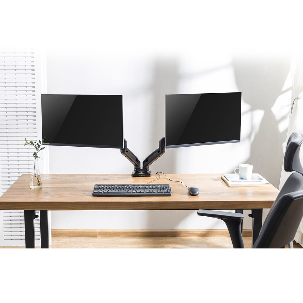 Een houten bureau met twee monitoren, toetsenbord en muis. Een stoel rechts. Een vaas met een plant links.