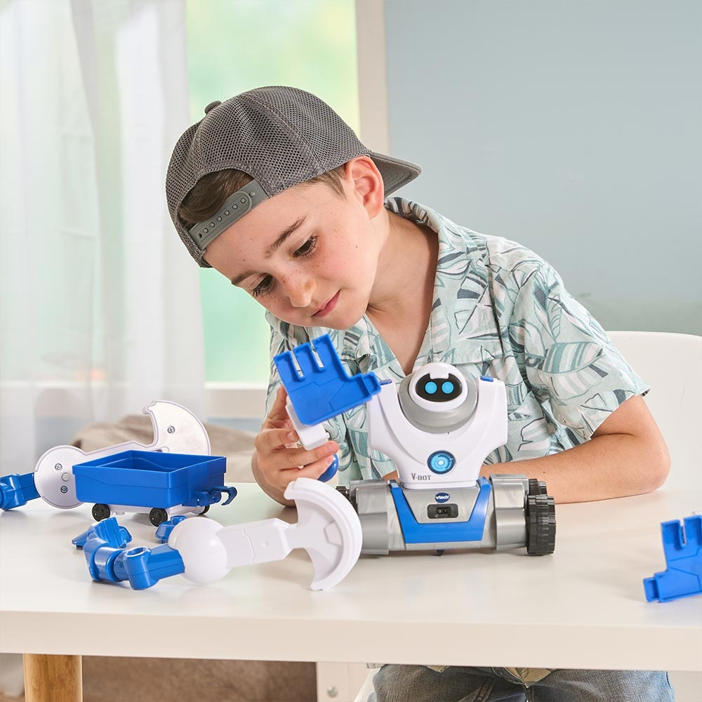 Un garçon avec une casquette assemble un robot jouet. Le robot est blanc et bleu. Il y a des pièces de robot sur la table.