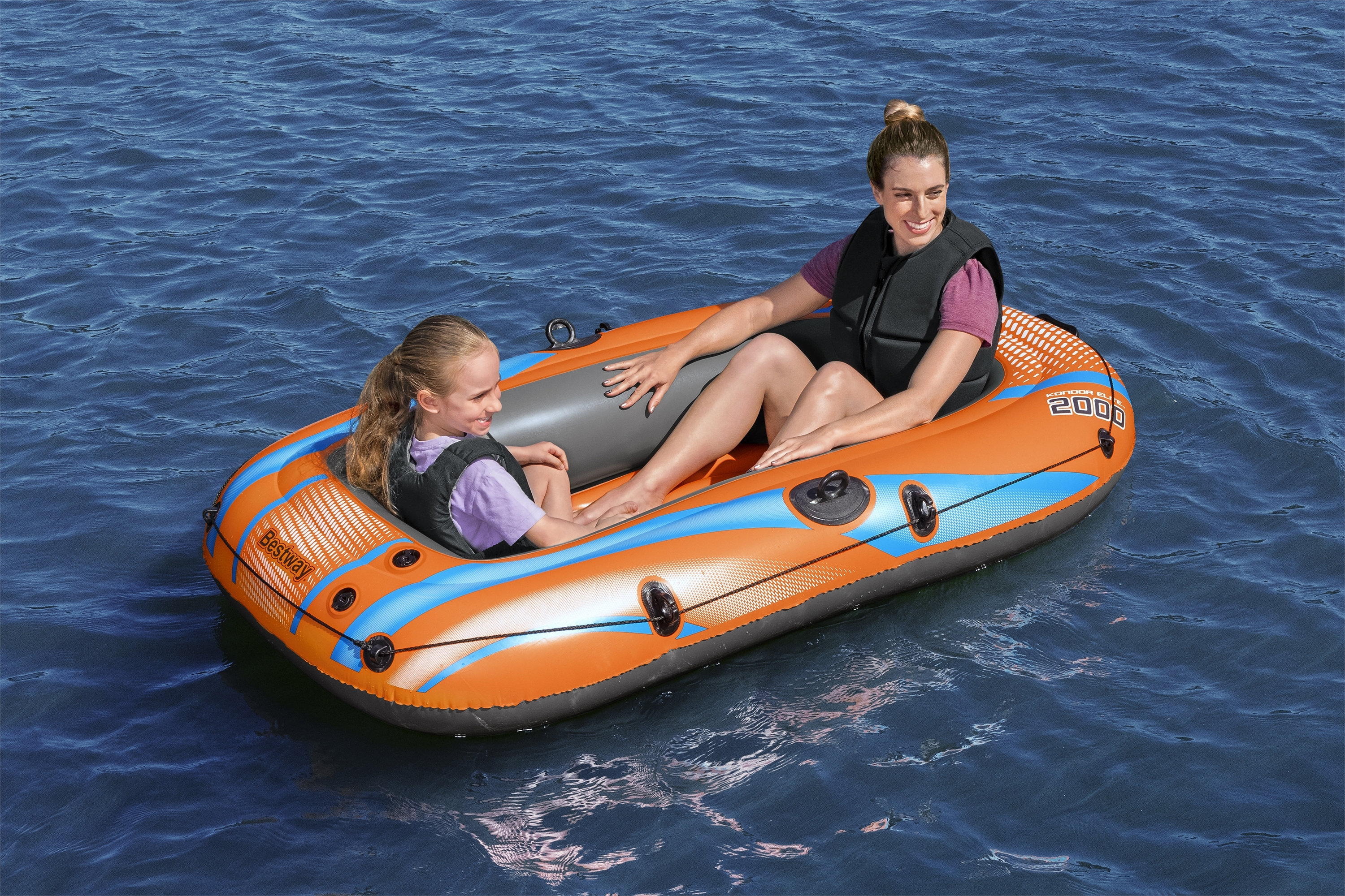 Zwei Frauen in einem orangefarbenen Schlauchboot auf blauem Wasser. Beide tragen Schwimmwesten. Eine lächelt.