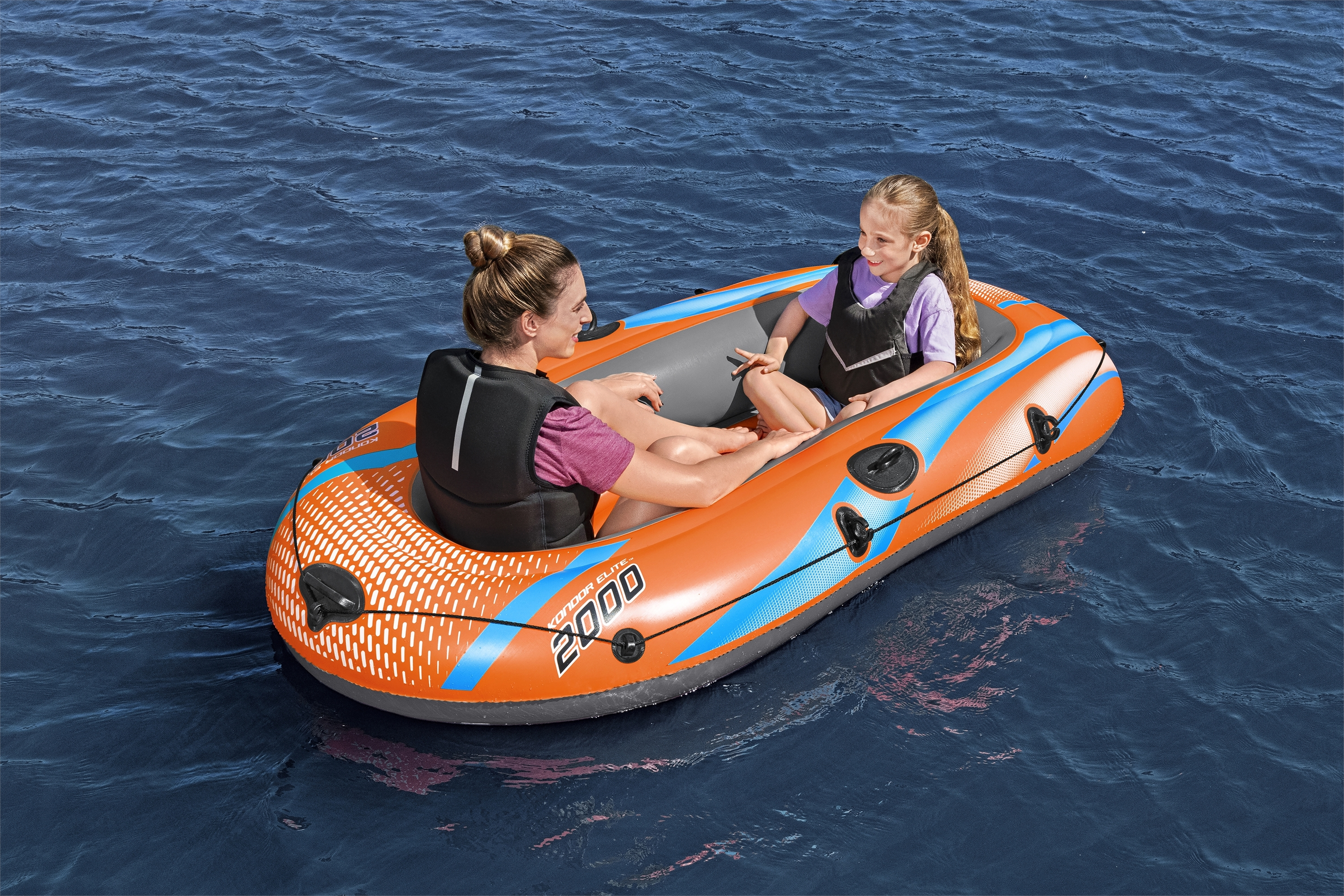 Zwei Personen in einem orangefarbenen Schlauchboot auf blauem Wasser. Beide tragen Schwimmwesten. Das Boot hat blaue Akzente.