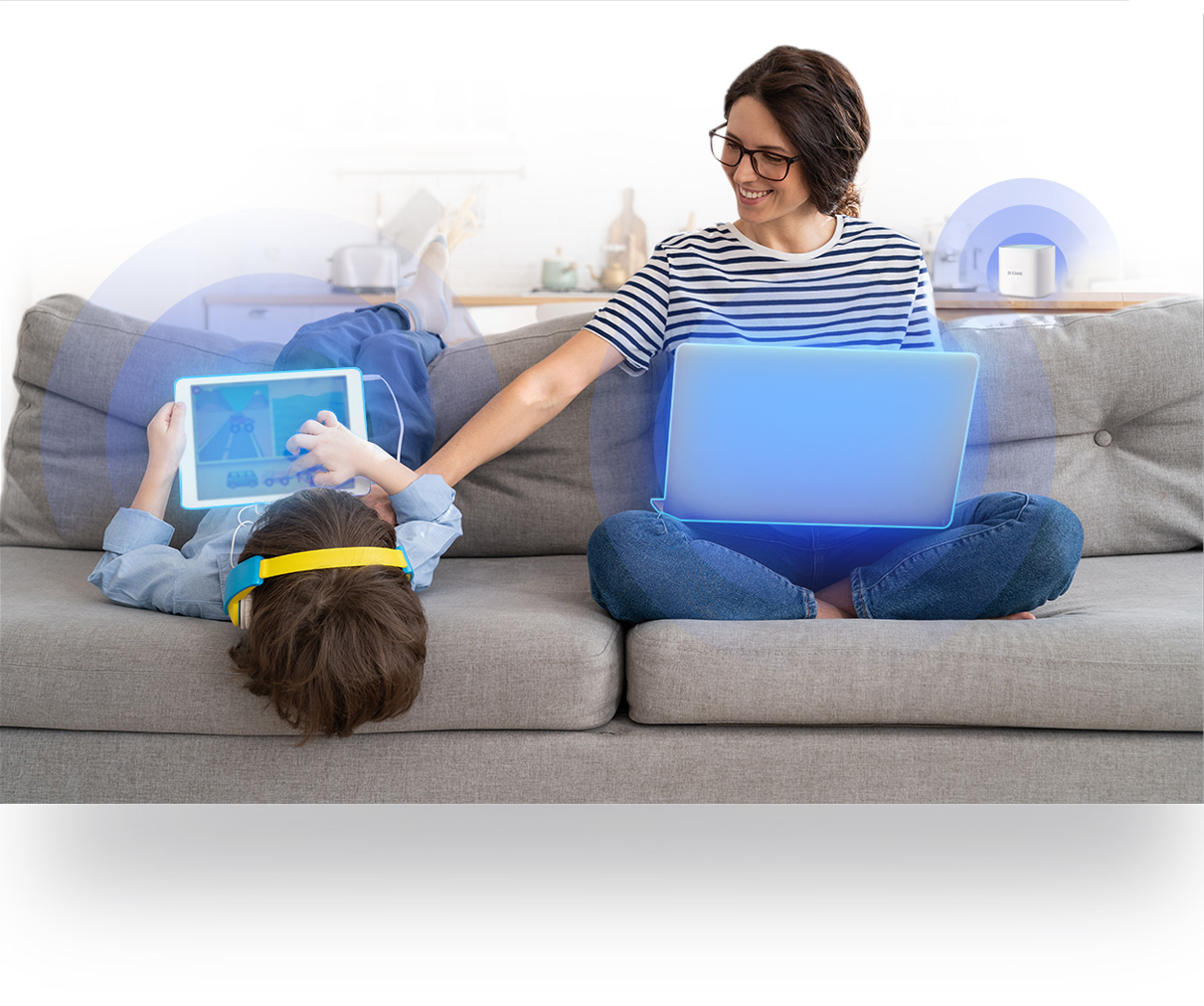 Kobieta i dziecko są na kanapie. Kobieta używa laptopa, dziecko tabletu ze słuchawkami. Oboje są połączeni.