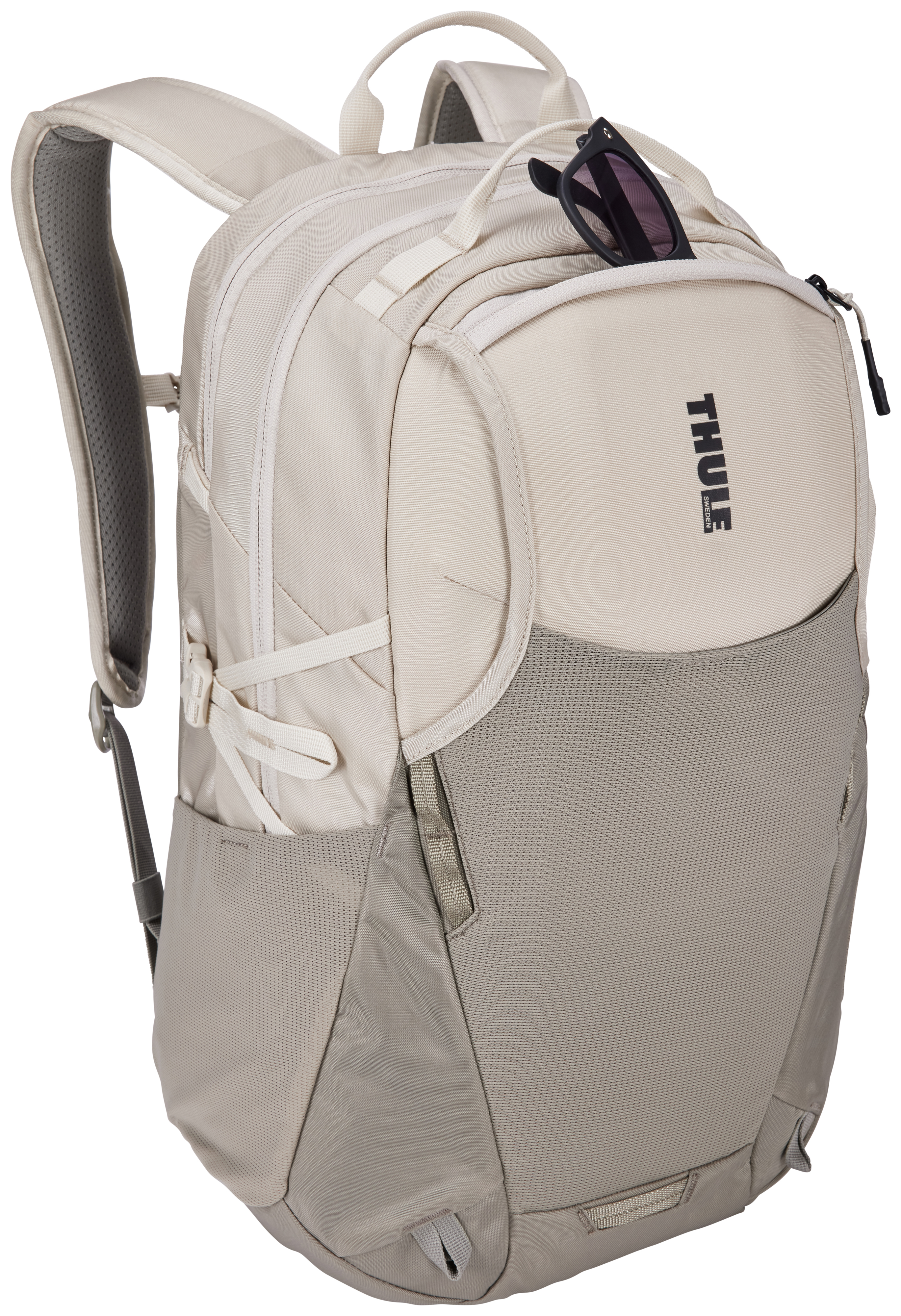Ein beiger Thule-Rucksack mit schwarzer Sonnenbrille in einer Tasche. Die Tasche befindet sich auf weißem Hintergrund.