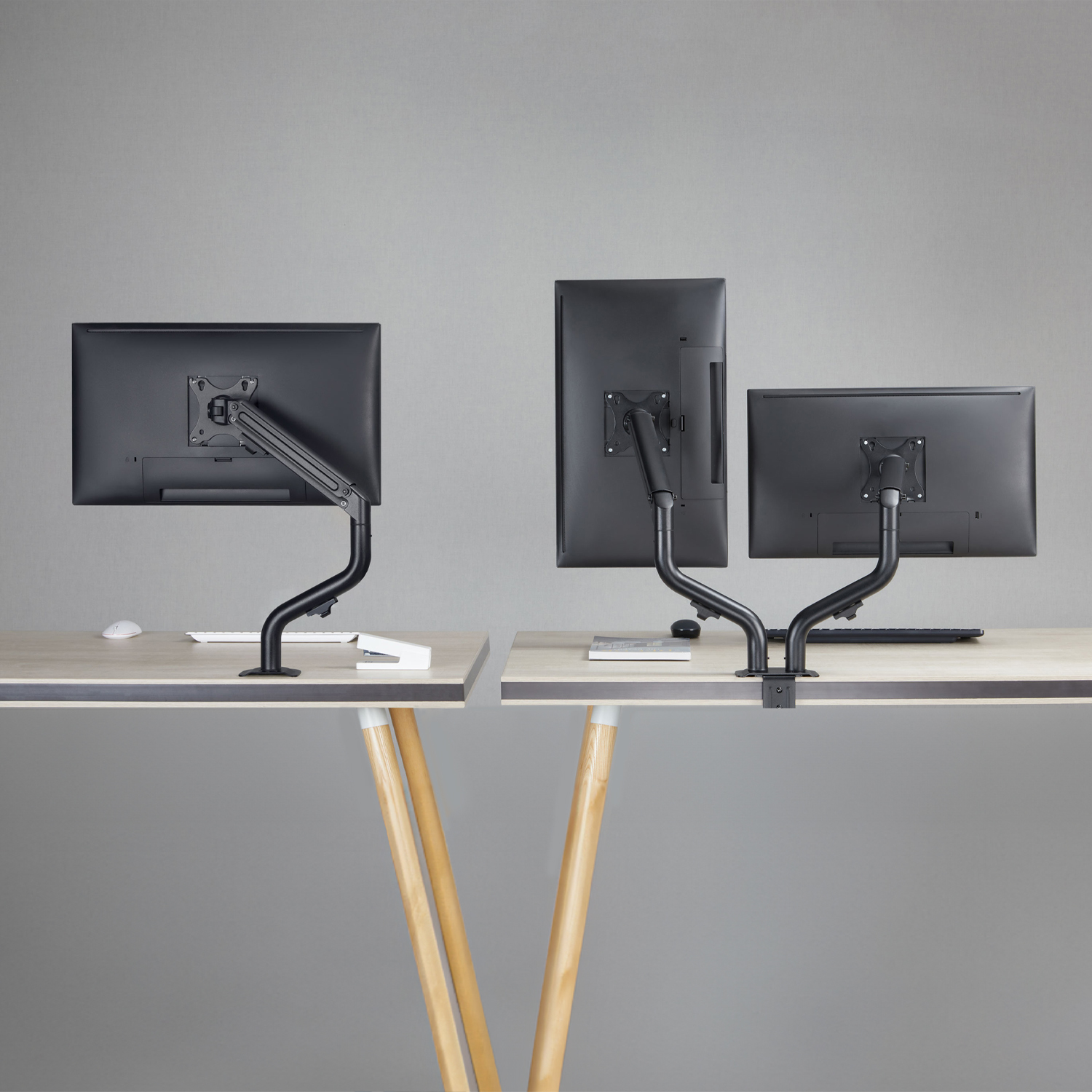 Trzy monitory komputerowe zamontowane na biurkach z czarnymi ramionami. Biurka są z jasnego drewna. Tło to szara ściana.