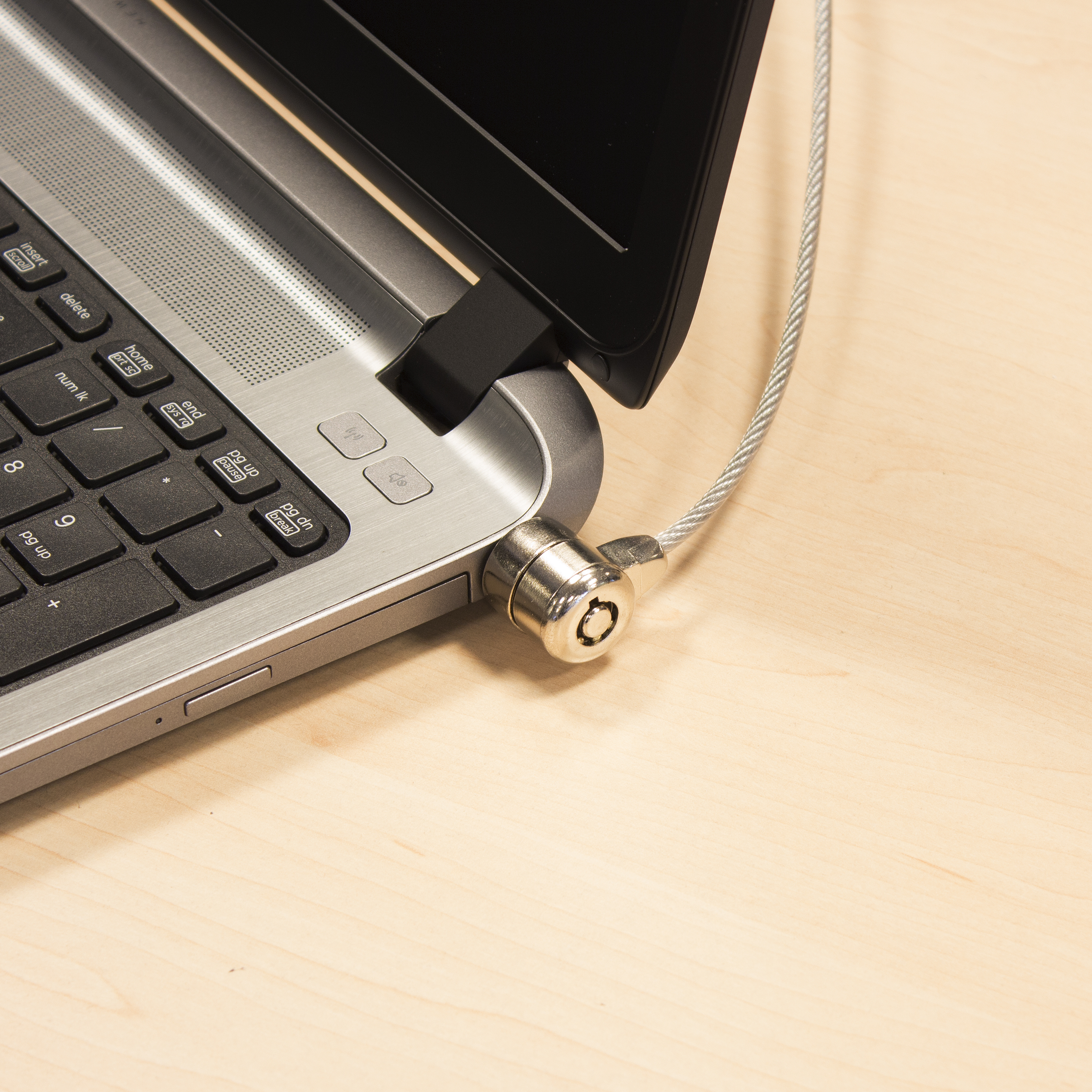 Portátil con cable de seguridad. Teclado, cerradura y parte de la pantalla. Fondo de madera clara.