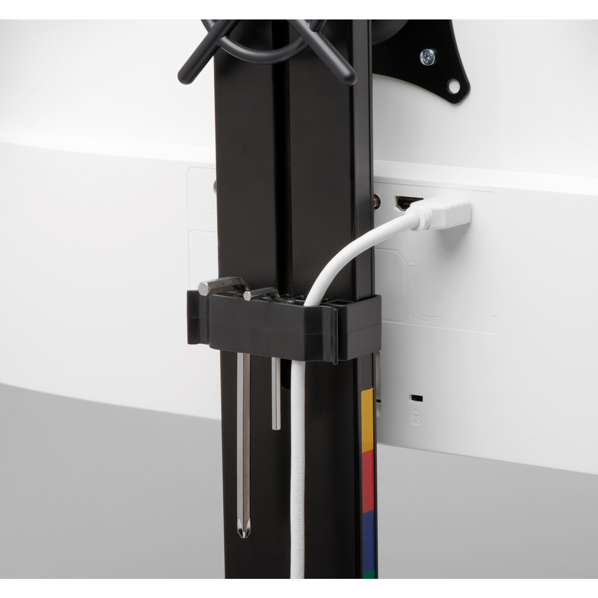 A white HDMI cable connected to a white monitor. A black bracket holds the cable. A black stand is on the left.