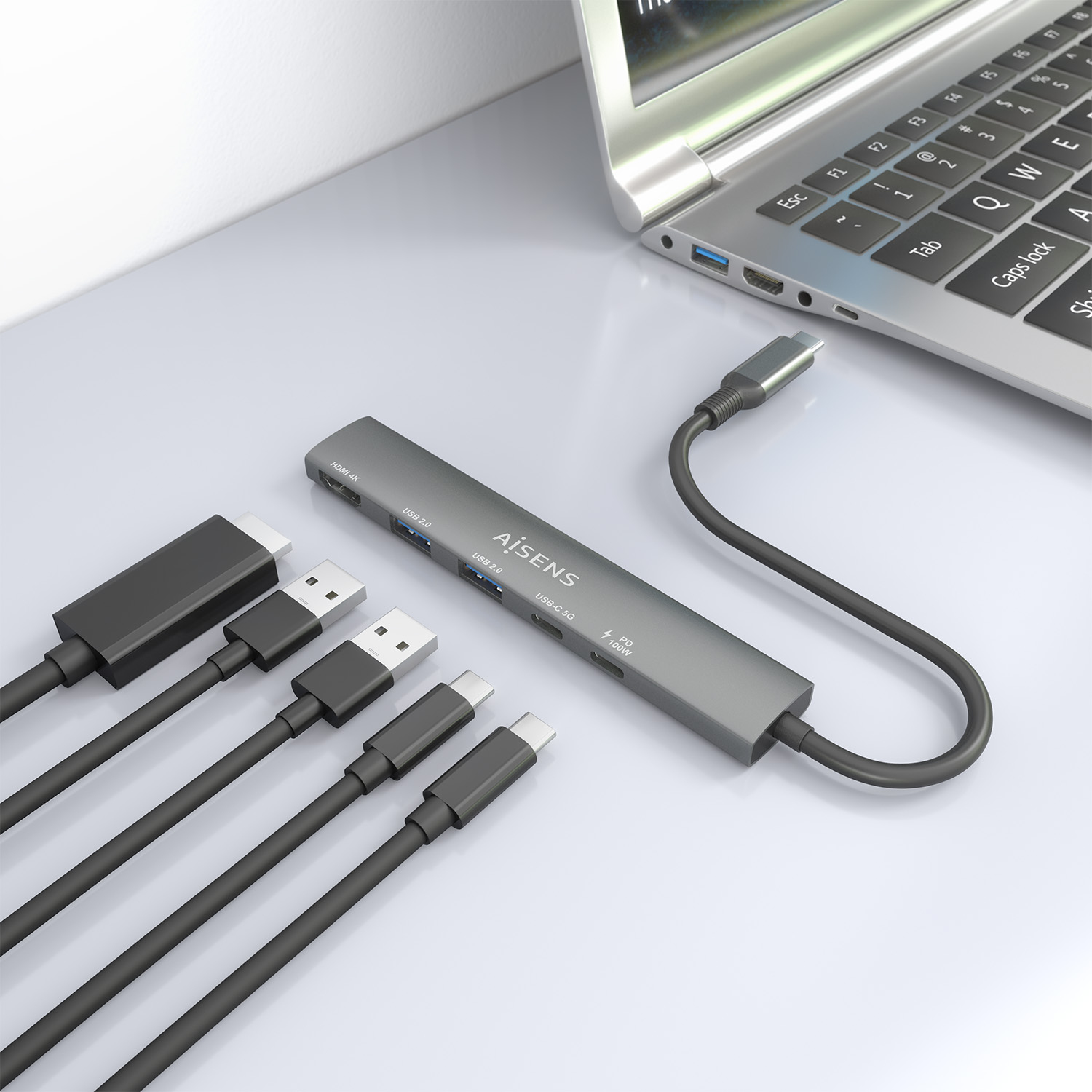 Un hub USB grigio con cavi collegati è accanto a un laptop. I cavi includono connettori USB, USB-C e HDMI.