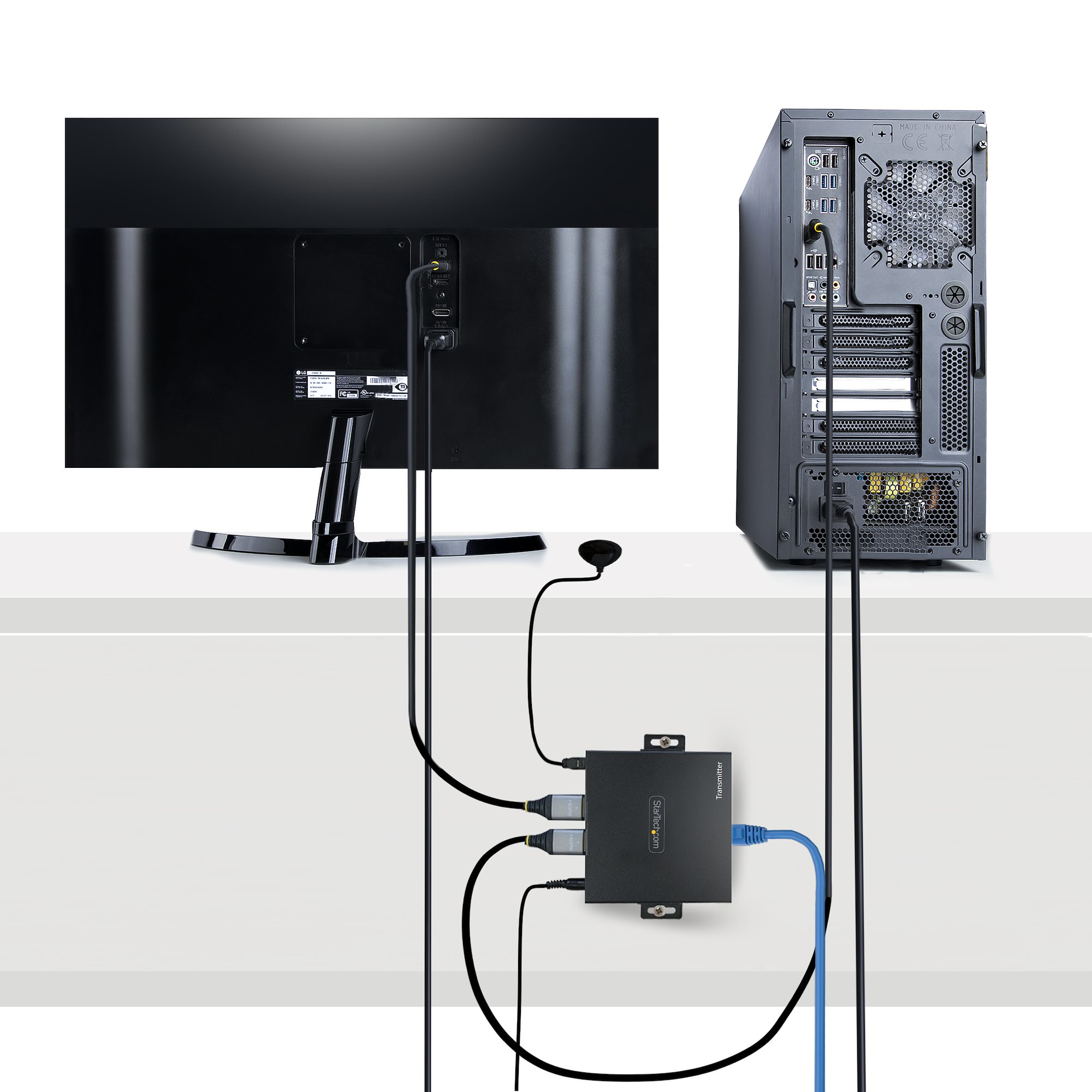 Rückseite eines Monitors, eines Computerturms und einer schwarzen Senderbox mit angeschlossenen Kabeln.